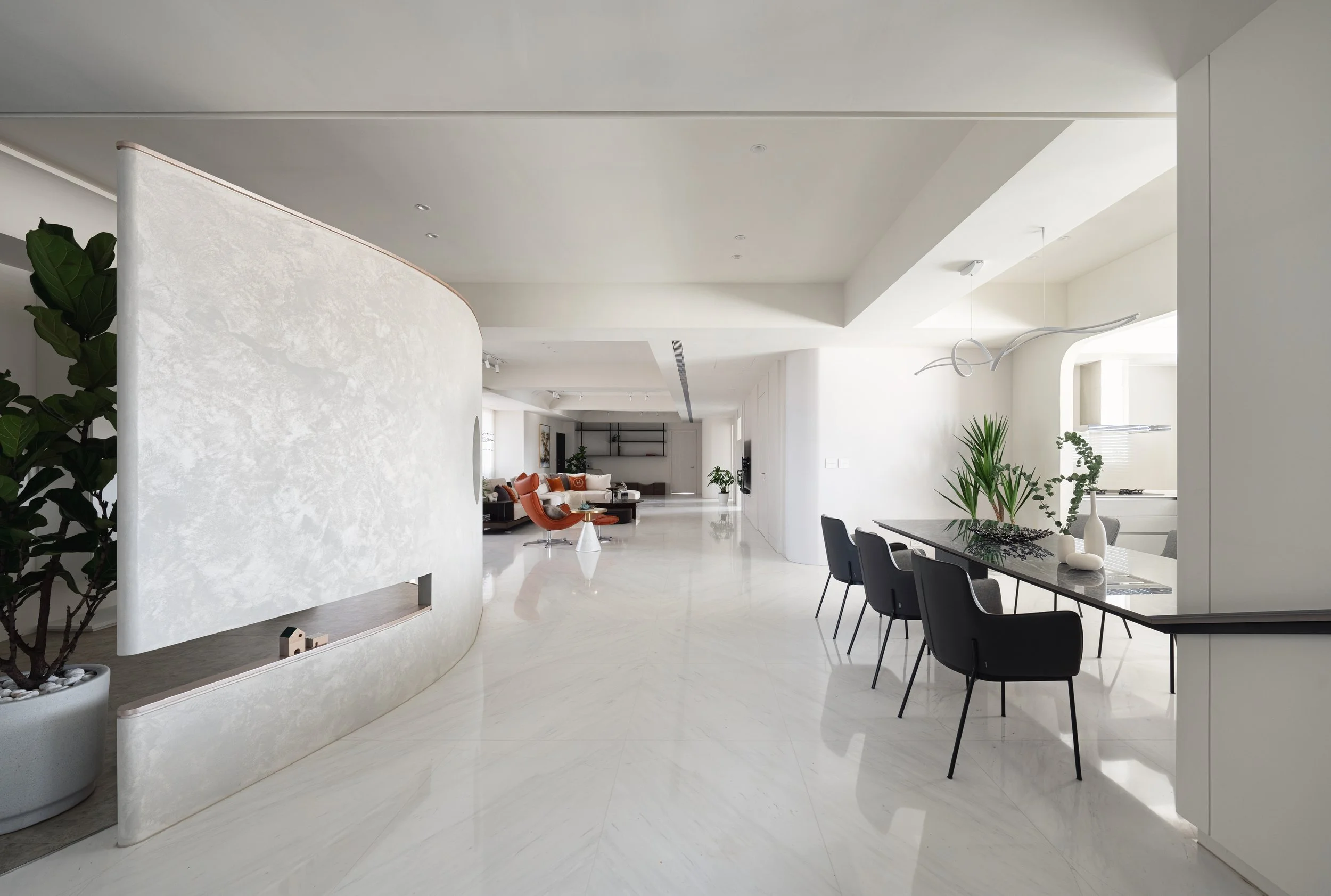Spacious modern living room with white walls and marble floor, featuring a black dining table with chairs, green plants, and minimalist decor.