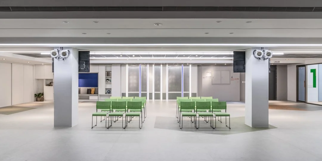 Modern church gathering space with green chairs, white floors and walls, and a cozy lounge area with cushions in the background, offering a calm and welcoming atmosphere for fellowship and reflection.