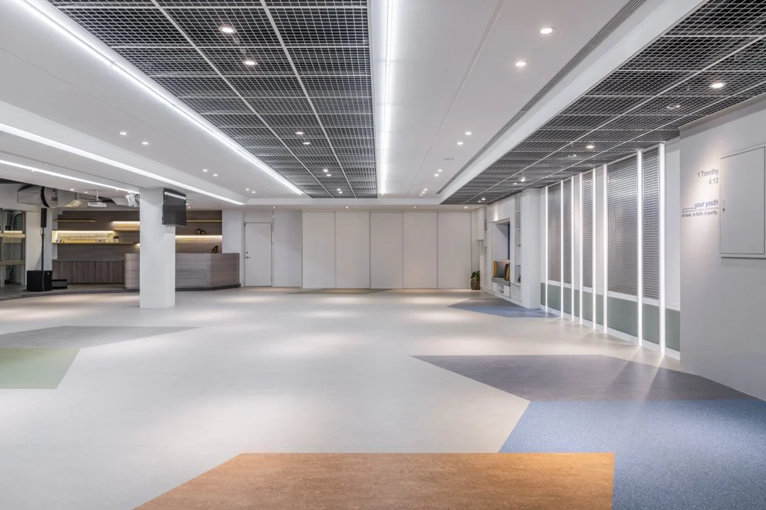 Modern and spacious lobby or waiting area featuring white walls, patterned ceiling panels, and multicolored floor tiles, offering a clean and welcoming environment.