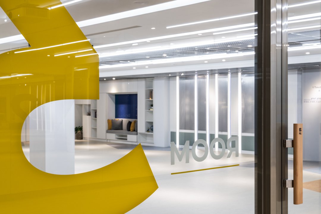 Modern church entrance lobby with white walls and a welcoming seating area, seen through a glass door adorned with a yellow graphic and the word “ROOM”, creating an inviting first impression for congregants and visitors alike.