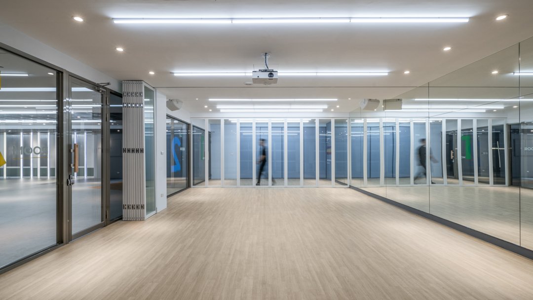 Modern multipurpose space in a church, featuring glass walls designed for dance rehearsals, sound-absorbing ceiling panels, and wood flooring, with a spacious layout that supports both gatherings and creative activities.