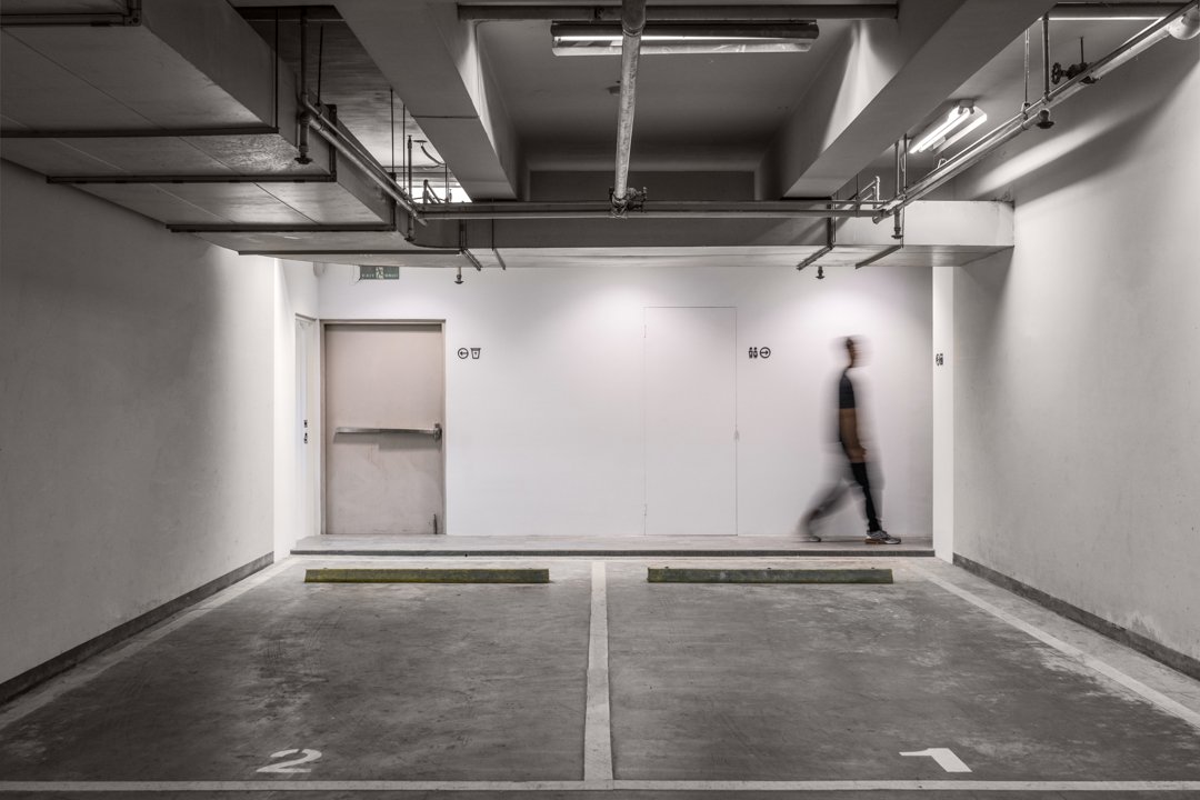 Underground parking garage with two empty parking spots numbered 1 and 2, with a blurred person walking past on the right side.