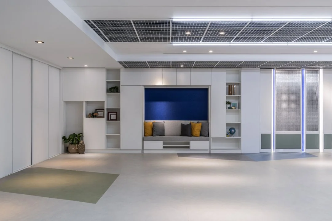 Modern reading nook in a church lobby, featuring built-in seating with yellow and gray pillows, decorative shelving, and glass sliding doors with blue accent panels — offering a quiet, inviting space for reflection and reading.