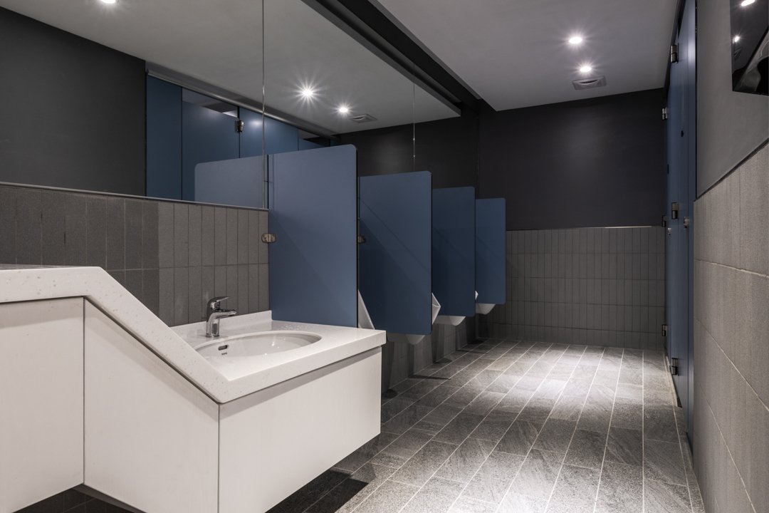 Public men's restroom with blue privacy stalls, a sink, and tiled floor.