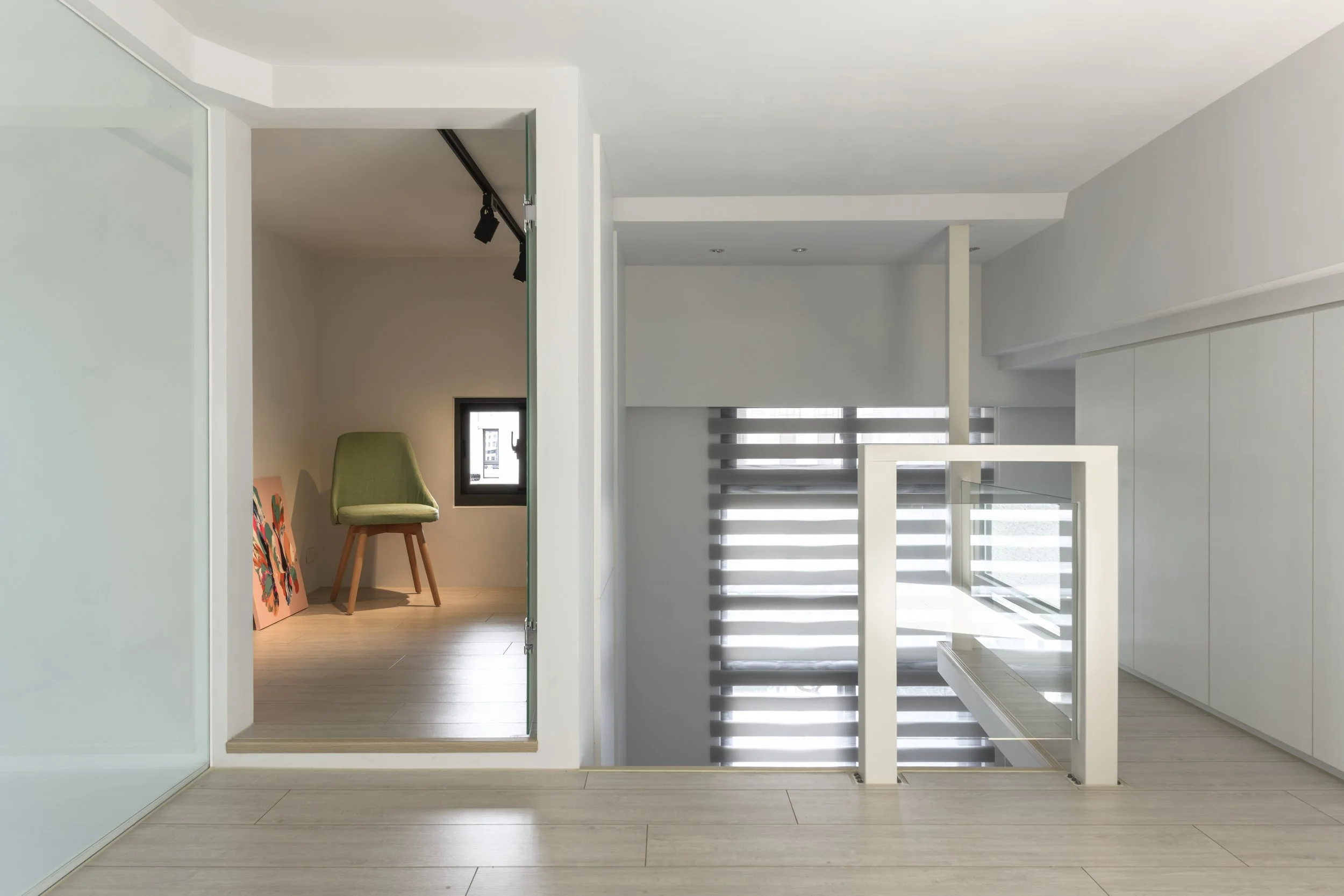 Modern interior with staircase, white walls, and a small room with a green chair and colorful paintings
