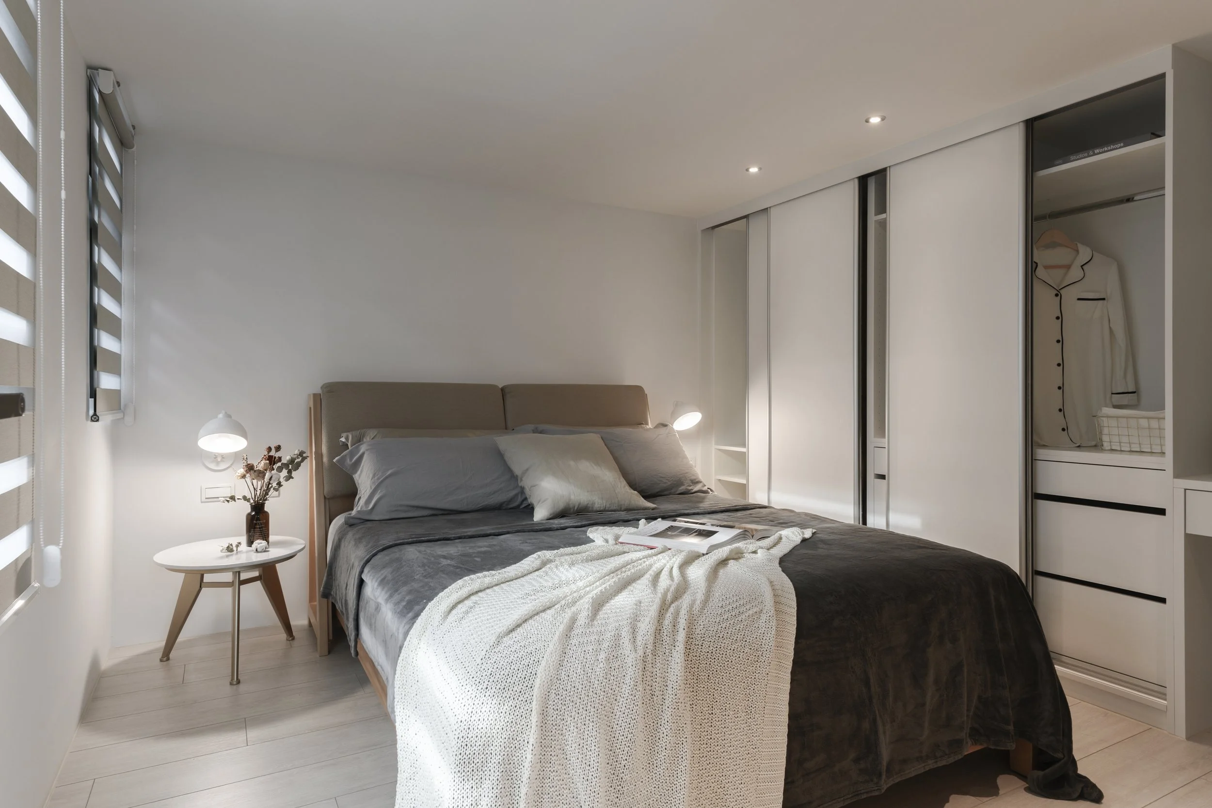 Modern bedroom with a bed, side table with a vase, and a closet with white sliding doors.