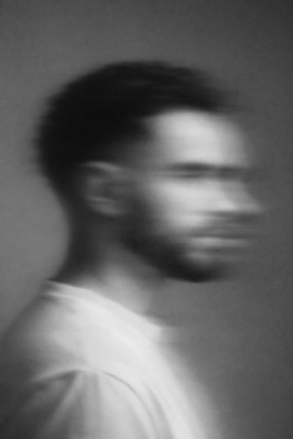 A black and white blurred profile of a person with short hair, wearing glasses and a light-colored shirt.