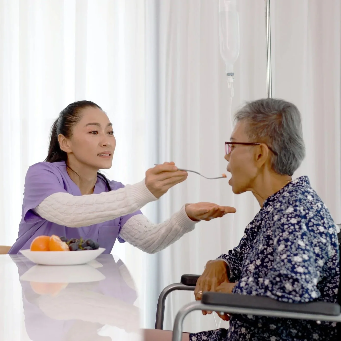 Nurse feeding a senior man yogurt in a cup, smiling at each other in a healthcare setting.