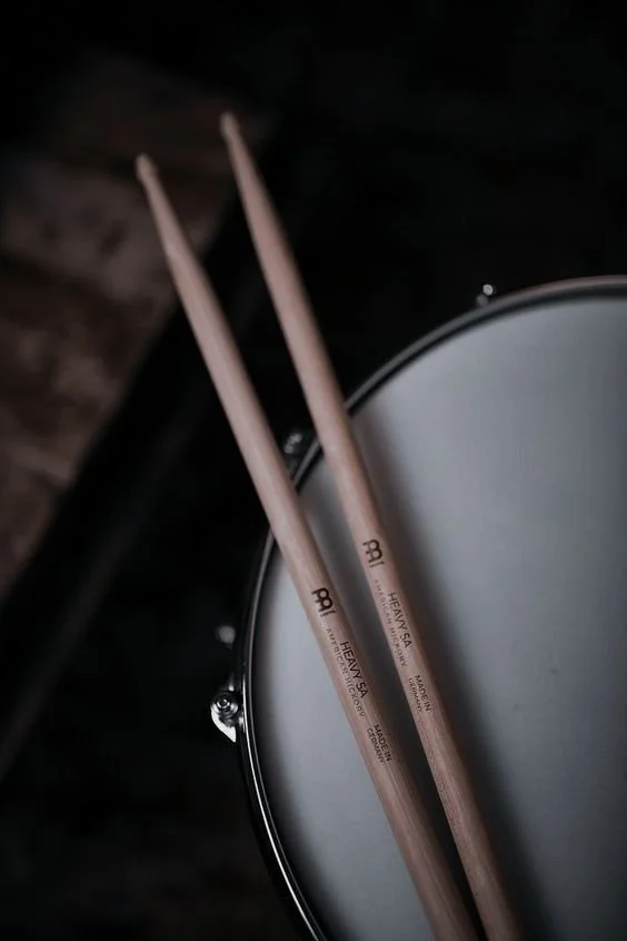 A pair of wooden drumsticks resting on a snare drum.