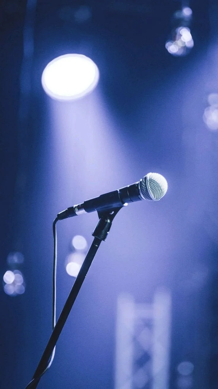 A microphone on a stand under stage lights with a blurred background.