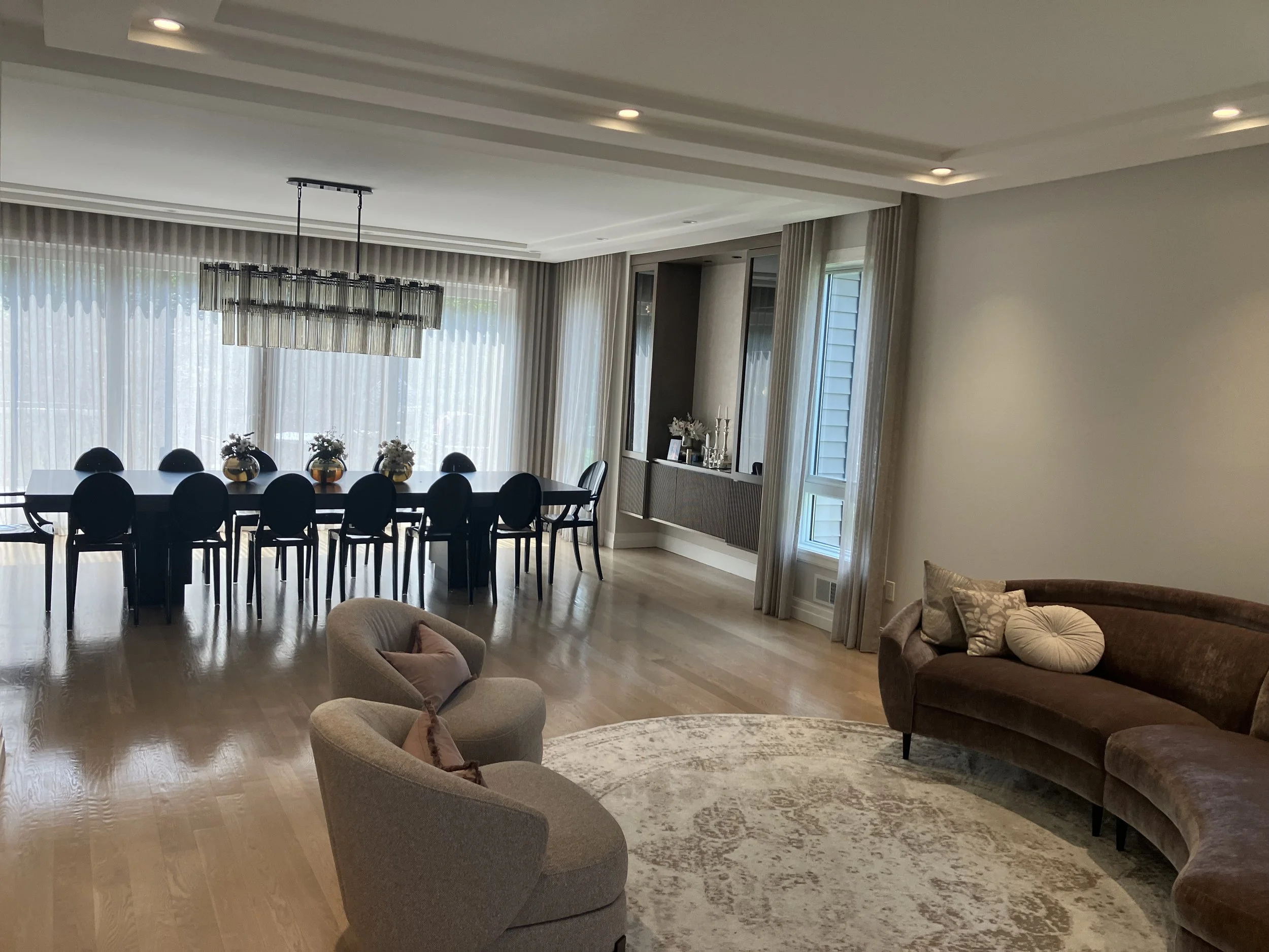 Elegant living and dining room with curved sofa, armchairs, dining table, and large windows with sheer curtains
