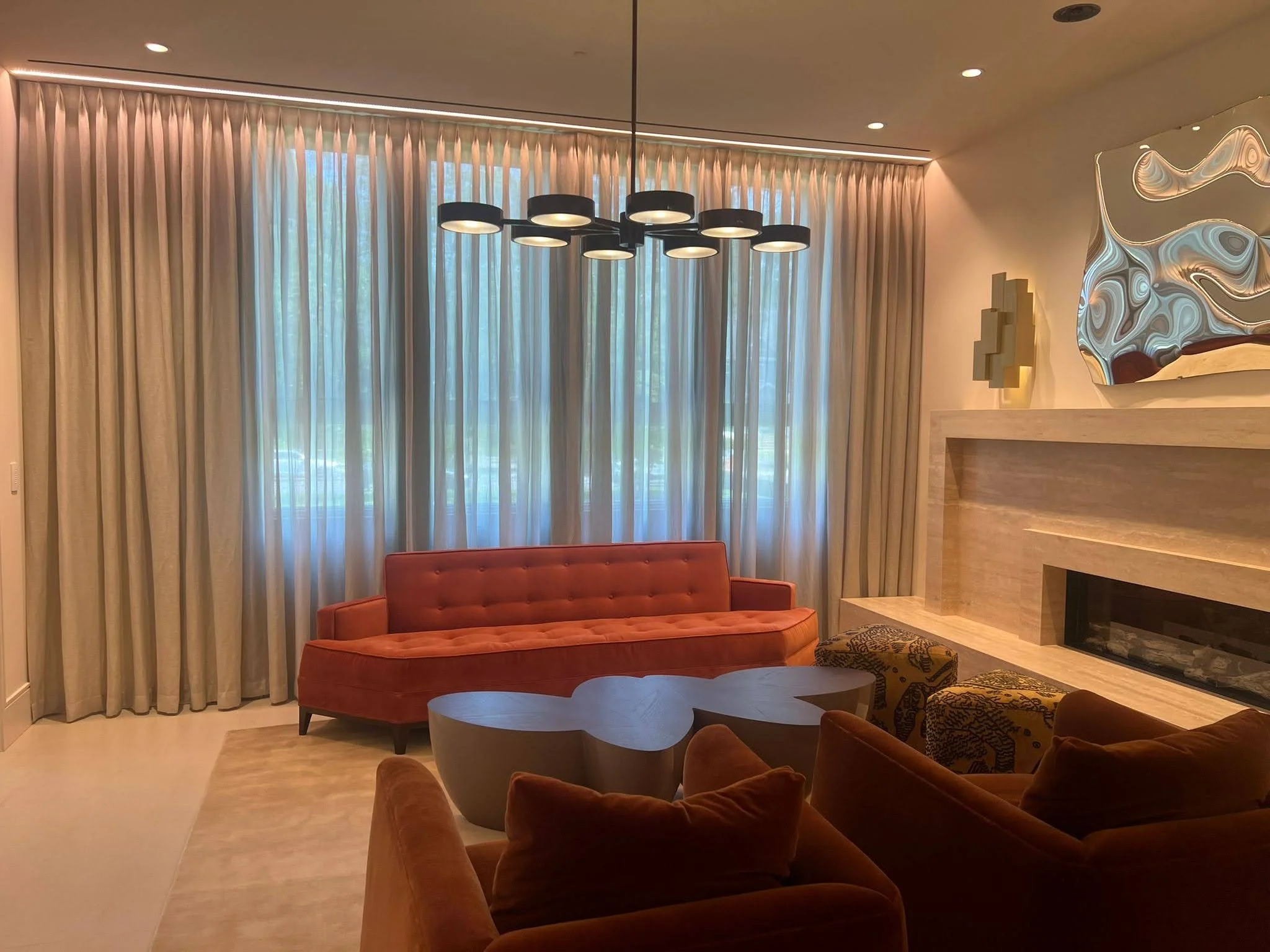 A living room with a red sofa, a wood coffee table, tan curtains, and modern decor including a fireplace and abstract artwork.