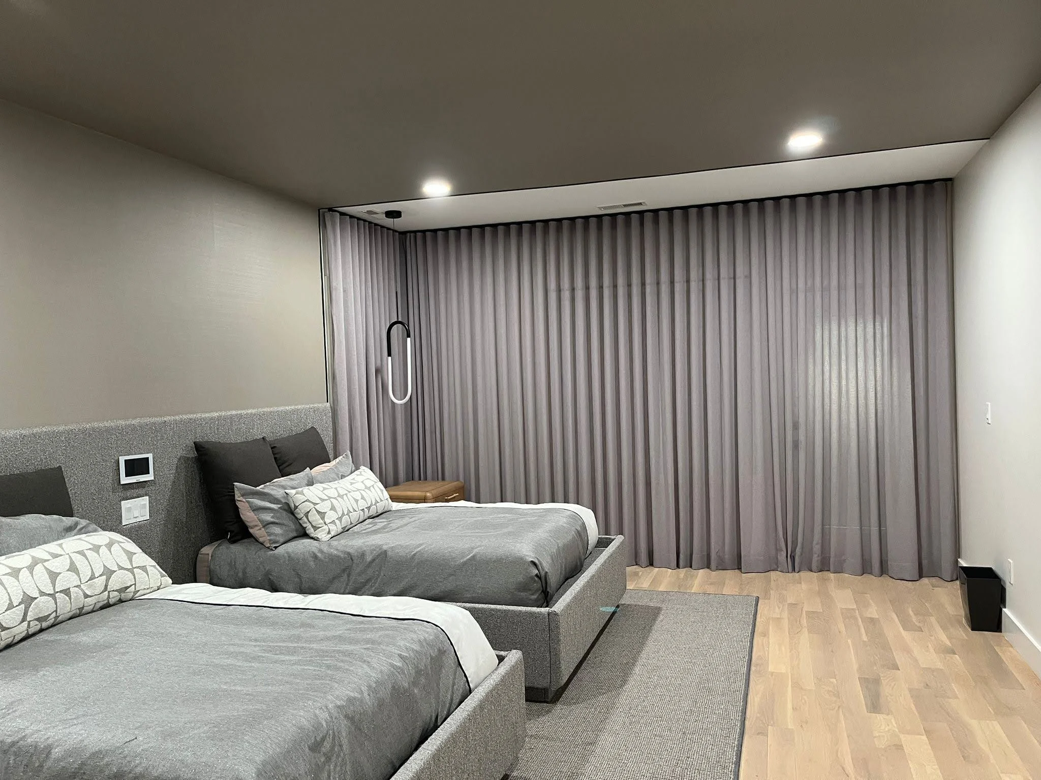 Modern bedroom with two beds, gray bedding, pillows, and gray curtains covering large window.