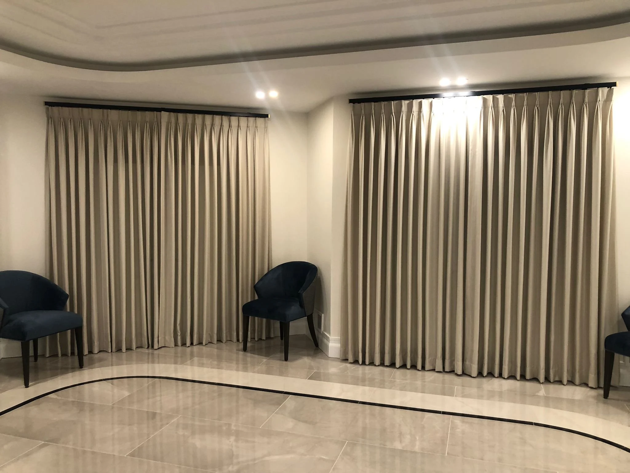 Room with beige curtains, two black chairs, and a tiled floor with black curved line design.