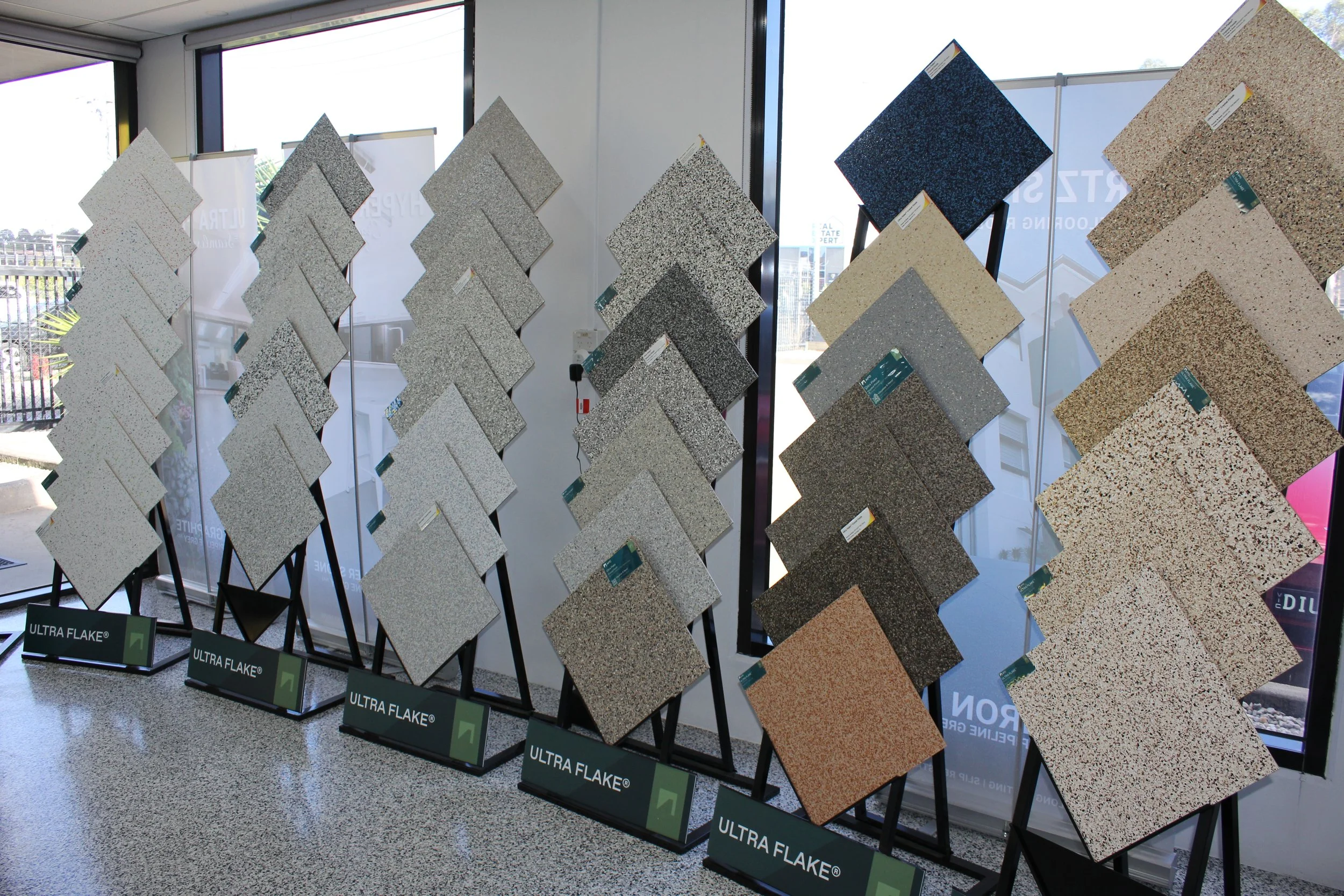 Display of various epoxy colour samples on stands with 'ULTRA FLAKE' 'HYPER FLAKE' branding, arranged in rows inside a store.