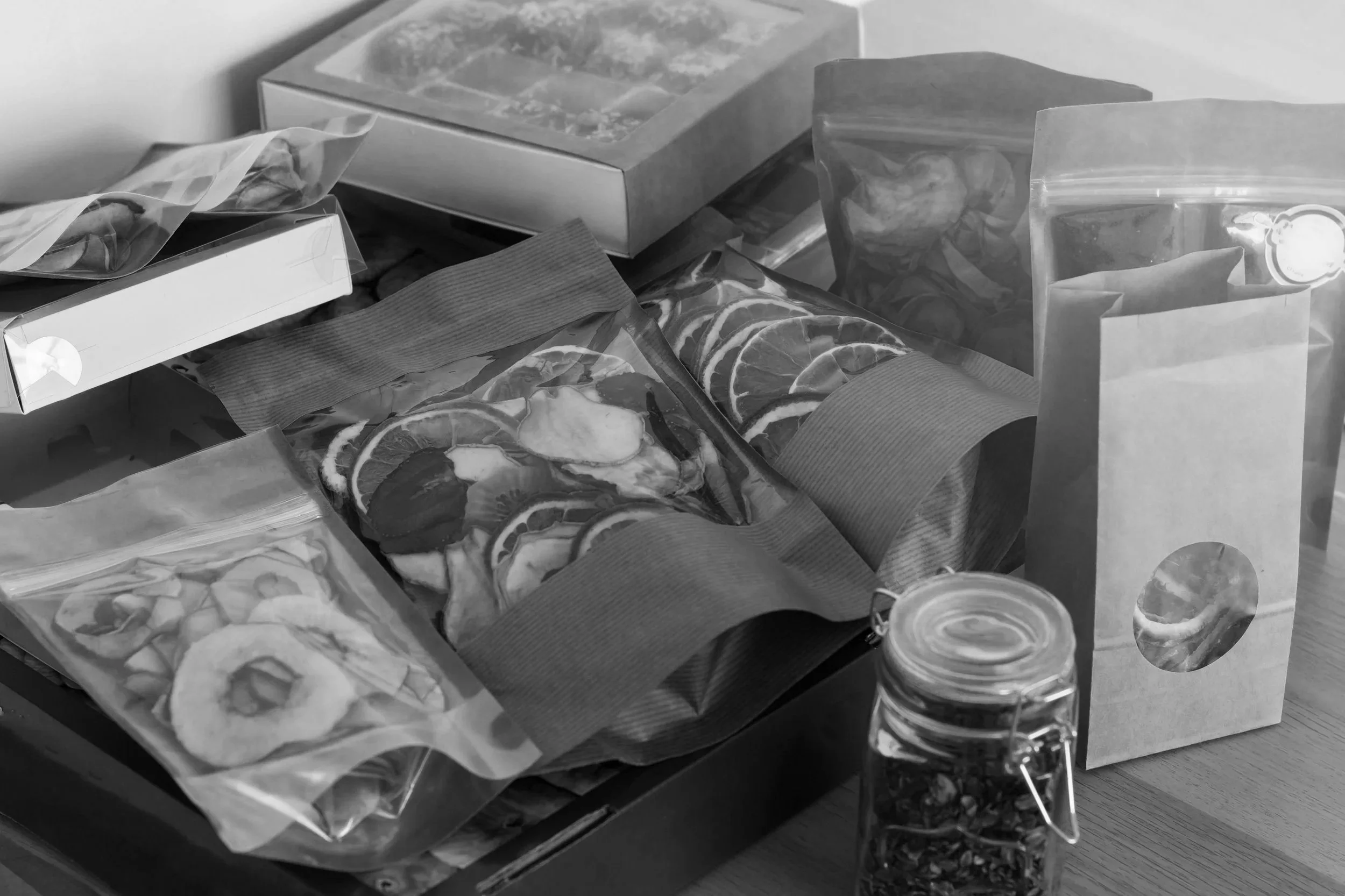 Assorted packaged dried fruit and snacks on a table, including sliced lemon or citrus, and a jar of dried herbs or fruit.