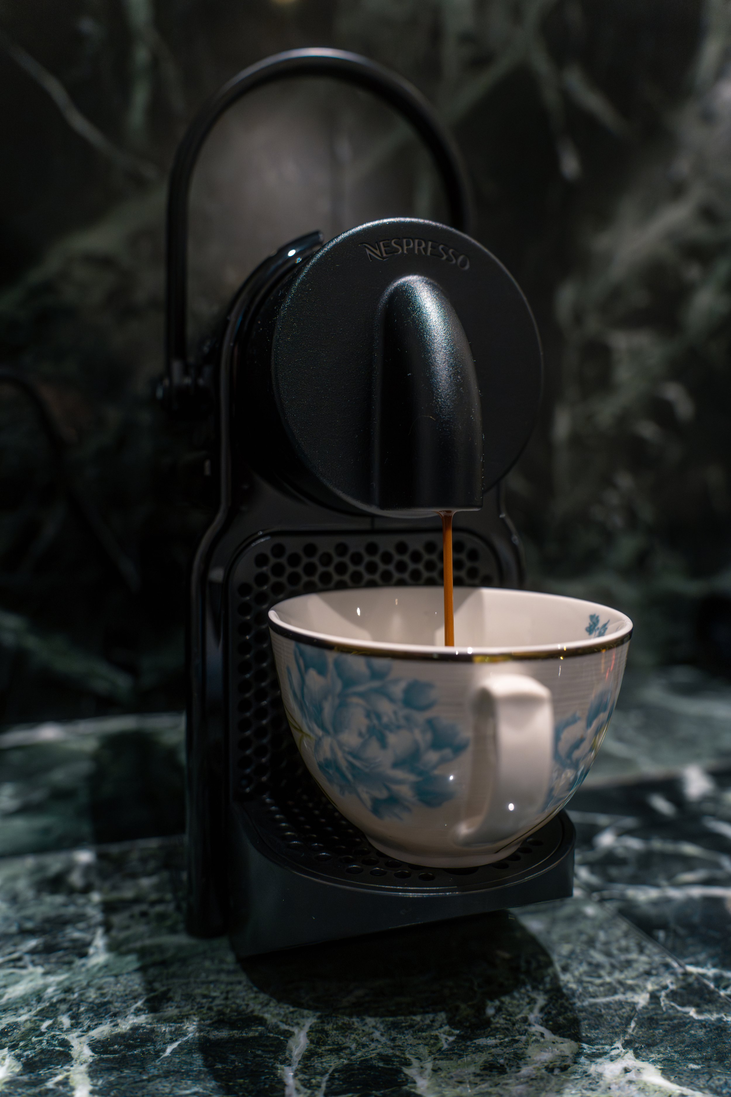 A Nespresso coffee machine brewing espresso into a patterned cup on a marble countertop.