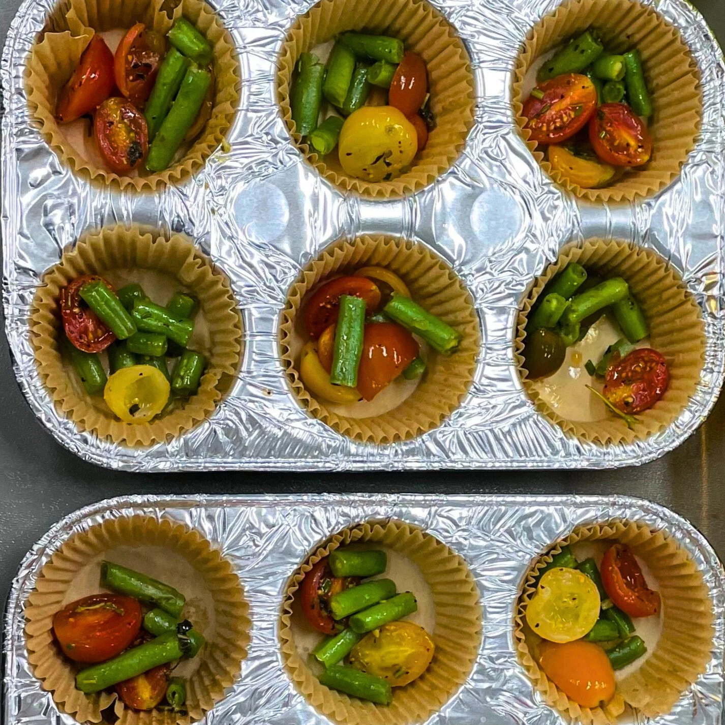 Nine cupcake liners filled with cherry tomatoes and green beans, placed on aluminum foil trays