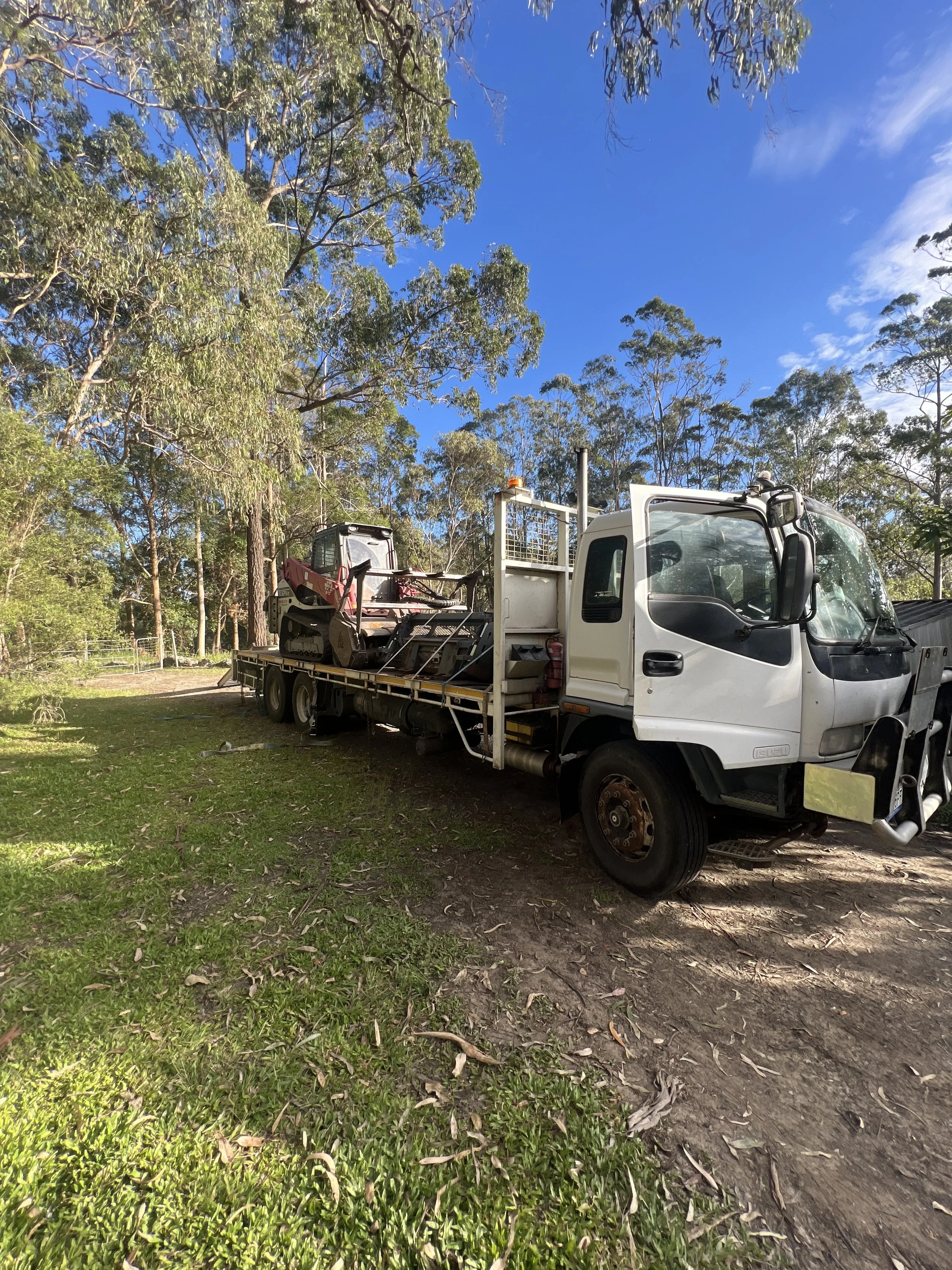 Fusion Forestry Mulching truck and low loader transporting the Fecon tracked mulcher to a South East Queensland job site, parked under eucalyptus trees ready for an orchard or plantation clearing project.