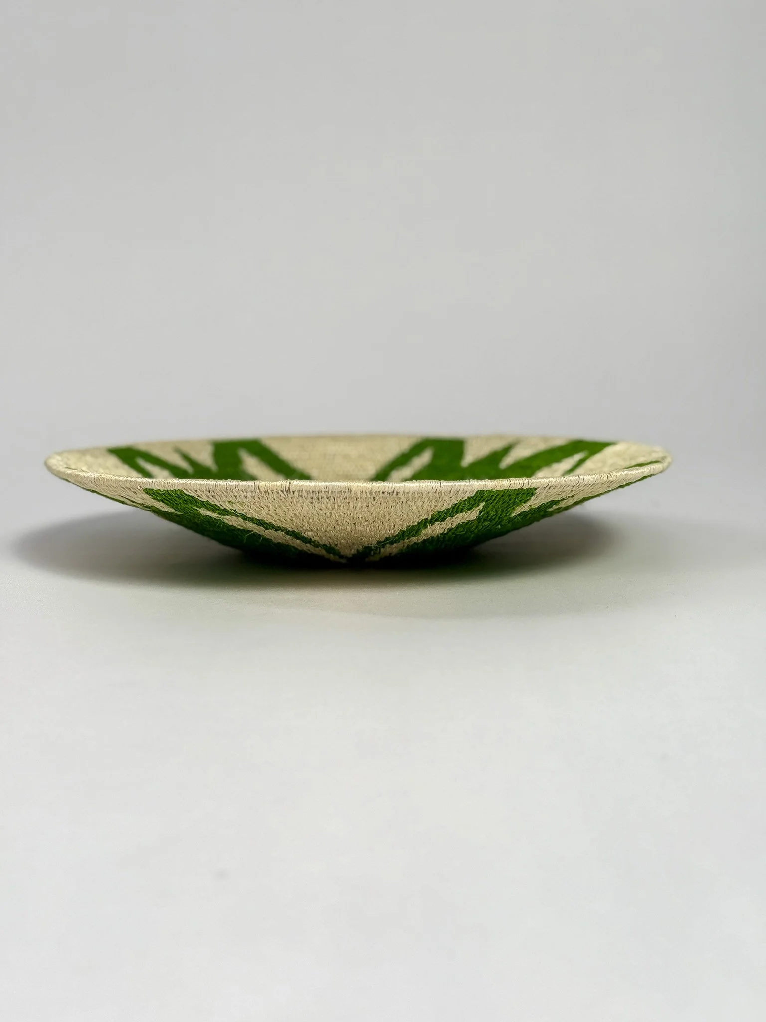Side view of a shallow ceramic bowl with green decorative pattern on a plain white background.