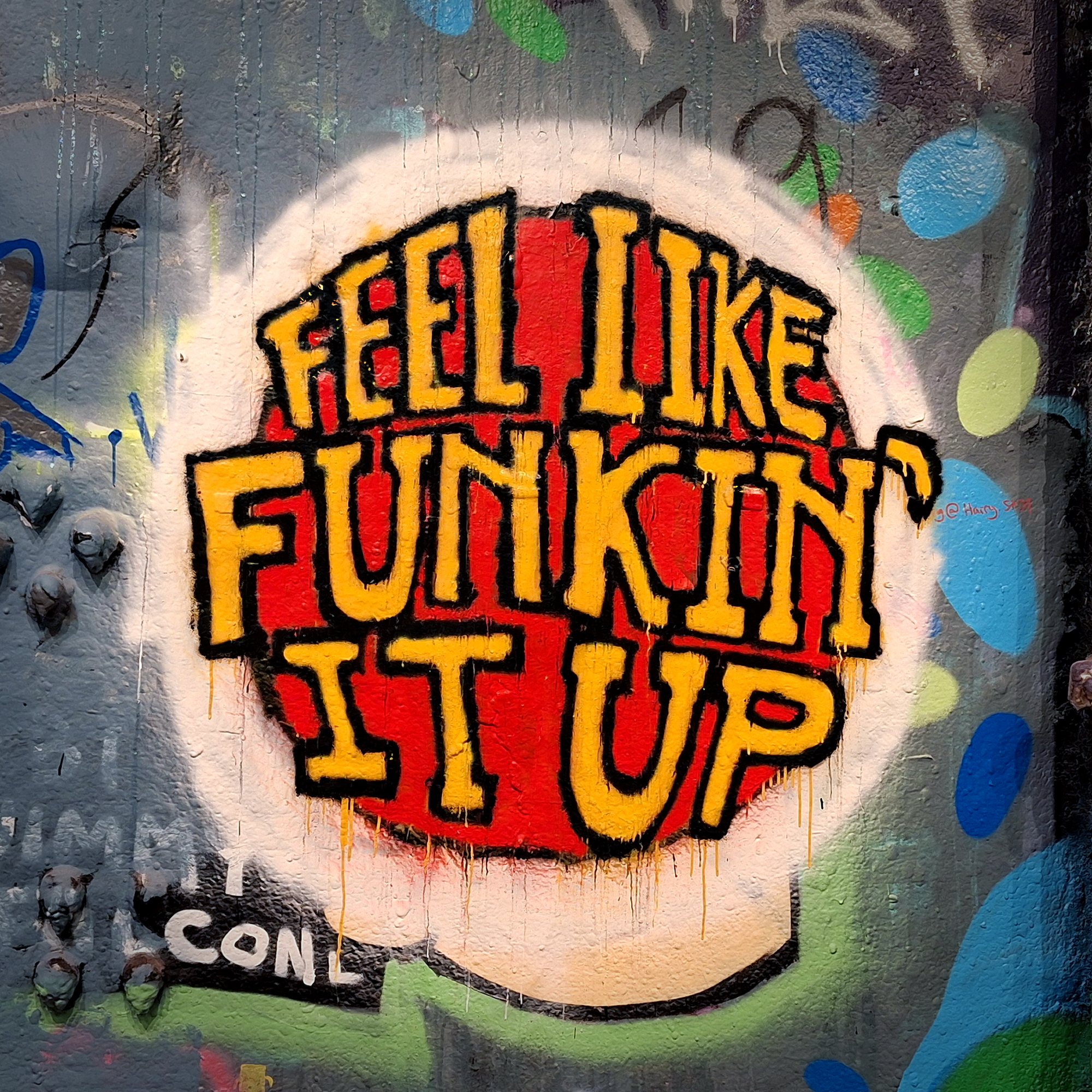 Graffiti art on a wall that reads, 'Feel like Funkin' It Up' in bold yellow and red letters, with colorful abstract background.