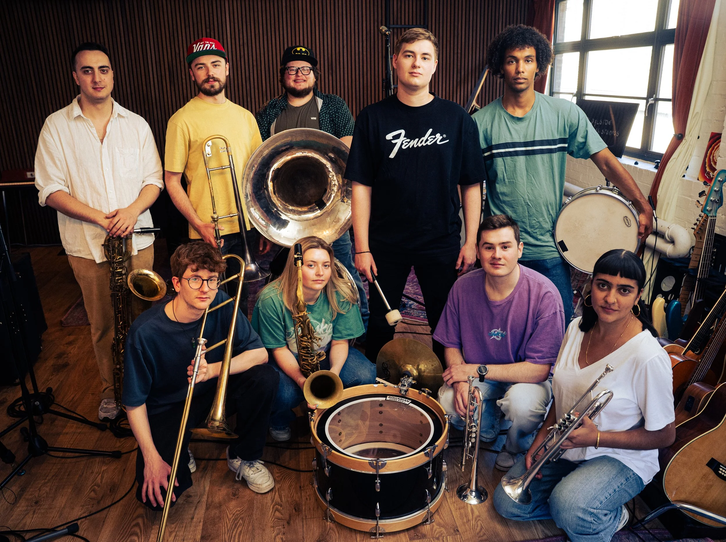 A group of nine diverse musicians with various instruments in a music studio