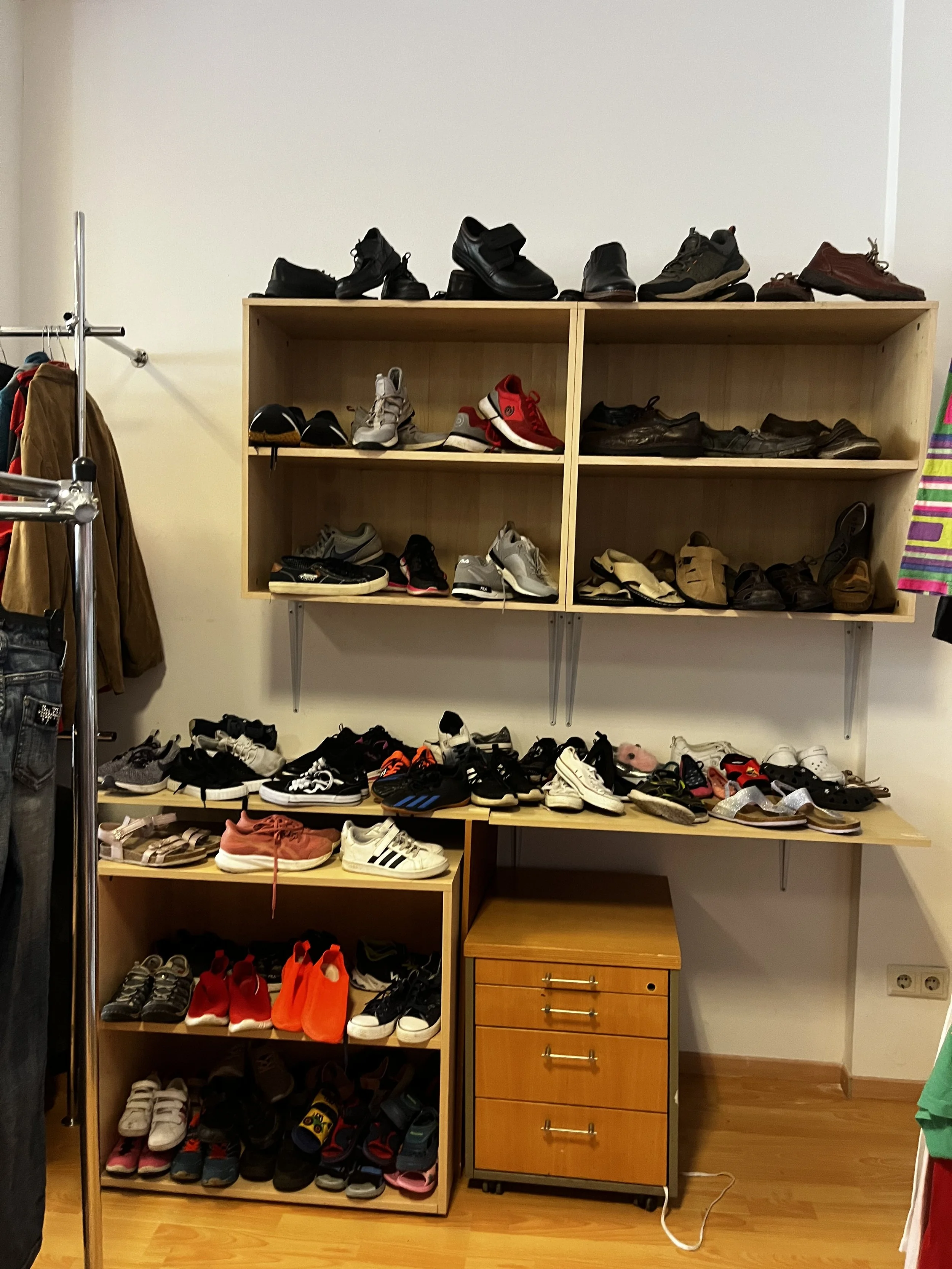 Sara Second Hand in Eisenhüttenstadt, Second Hand & Vintage Mode für alle. Kleidung, Haushaltsartikel & Accessories. Ein Holzregal, die mit verschiedenen Männer Schuhen gefüllt sind, in einer Ecke eines Raumes mit Holzfußboden.