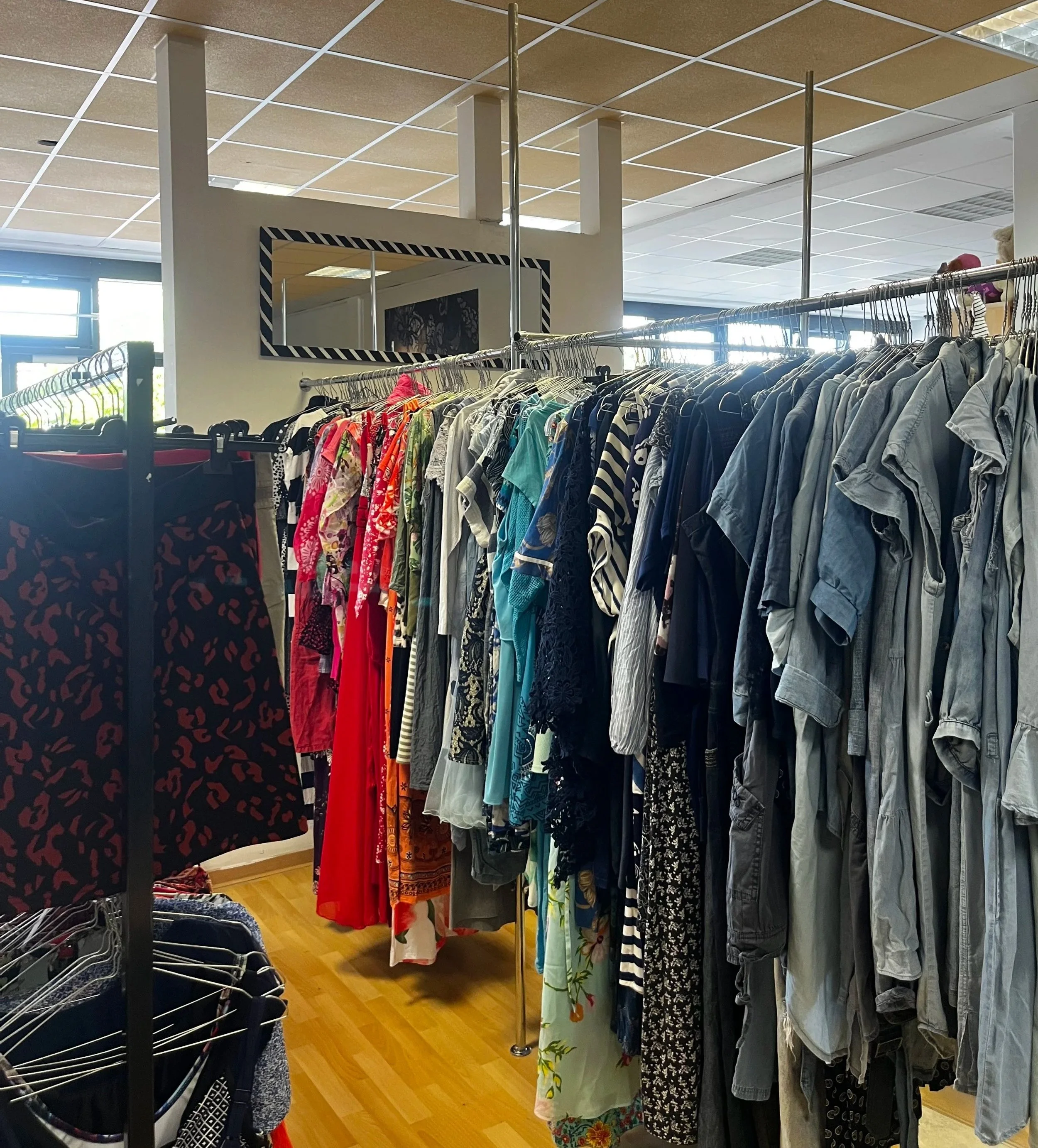 Sara Second Hand in Eisenhüttenstadt, Second Hand & Vintage Mode für alle. Kleidung, Haushaltsartikel & Accessories. Kleidungsstangen mit verschiedenen Kleidern für jeden Anlass n einem Secondhand-Shop.