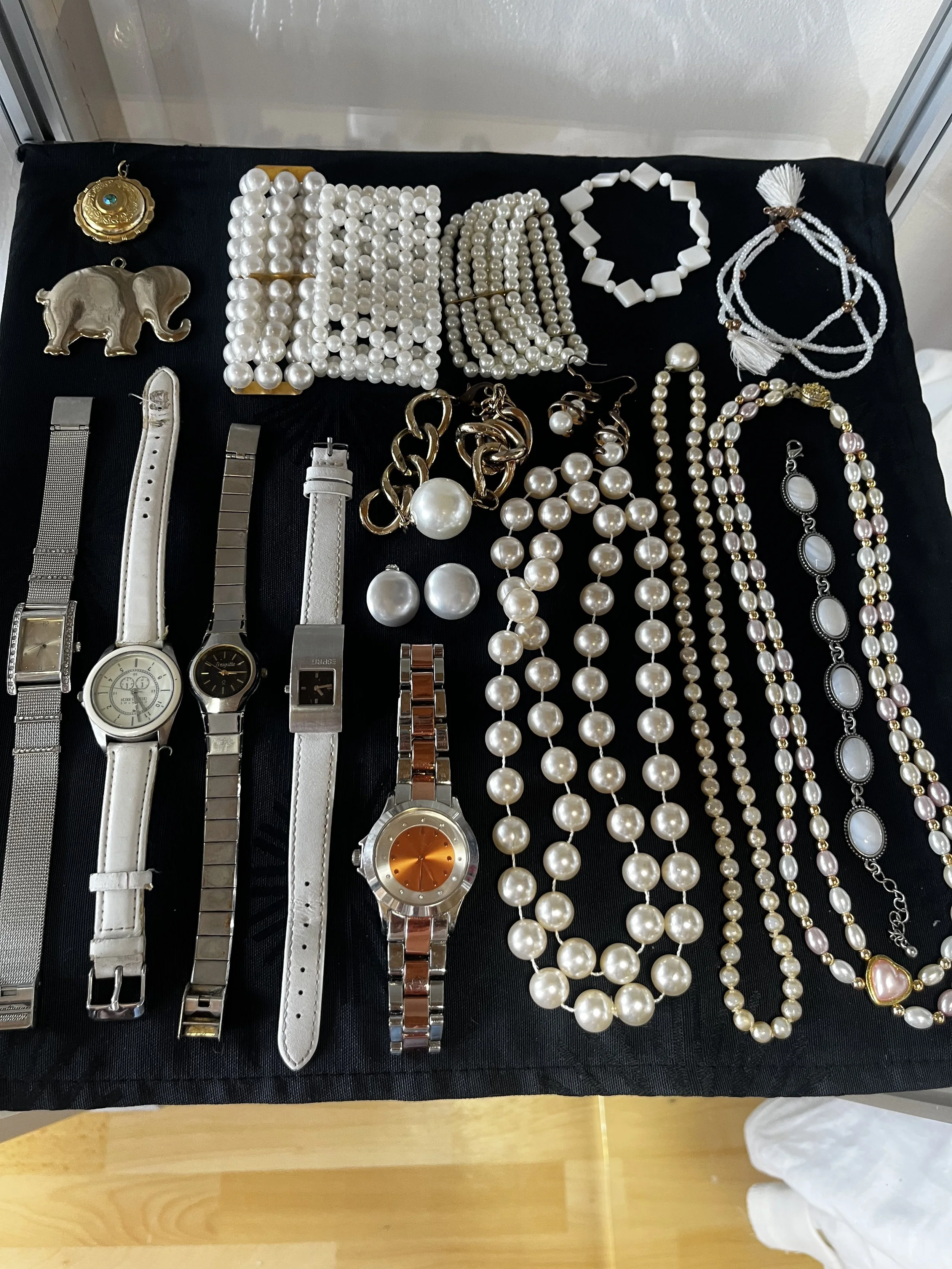 Sara Second Hand in Eisenhüttenstadt, Second Hand & Vintage Mode für alle. Kleidung, Haushaltsartikel & Accessories. Verschiedene Schmuckstücke und Uhren auf einem schwarzen Tuch, darunter Halsketten, Armbänder, Ohrringe, Uhren und Broschen.