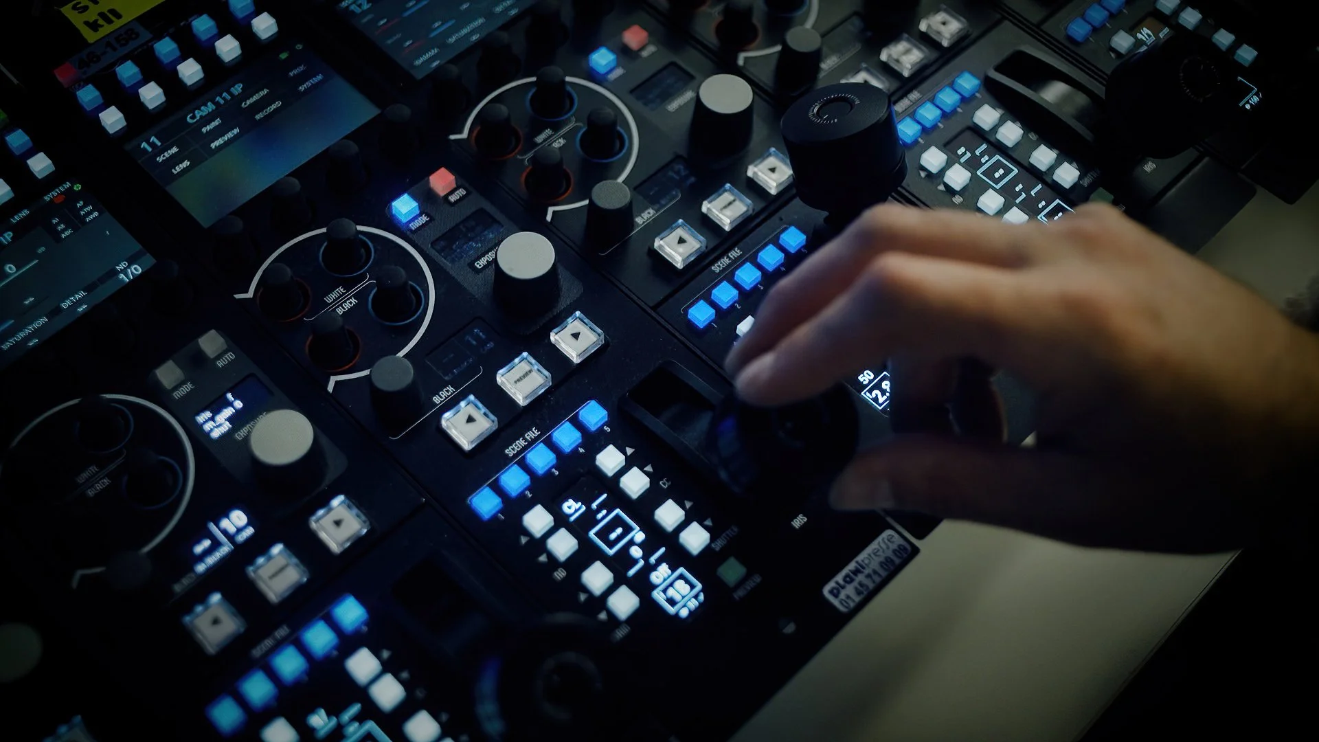 A DJ's hand adjusting a control knob on a professional music mixing console with illuminated buttons and screens.