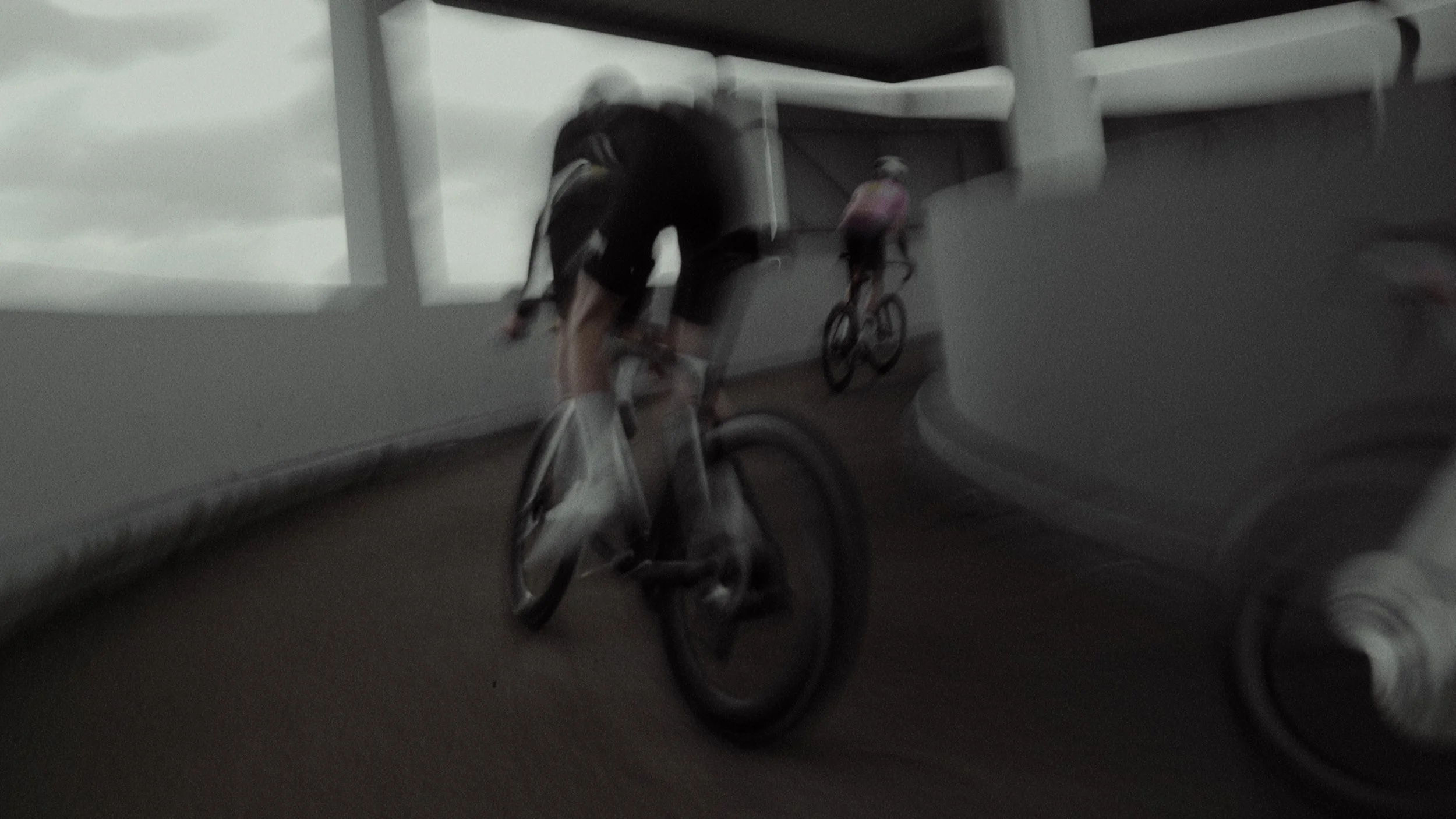Two cyclists riding on a bridge or elevated pathway, with clouds visible in the background.
