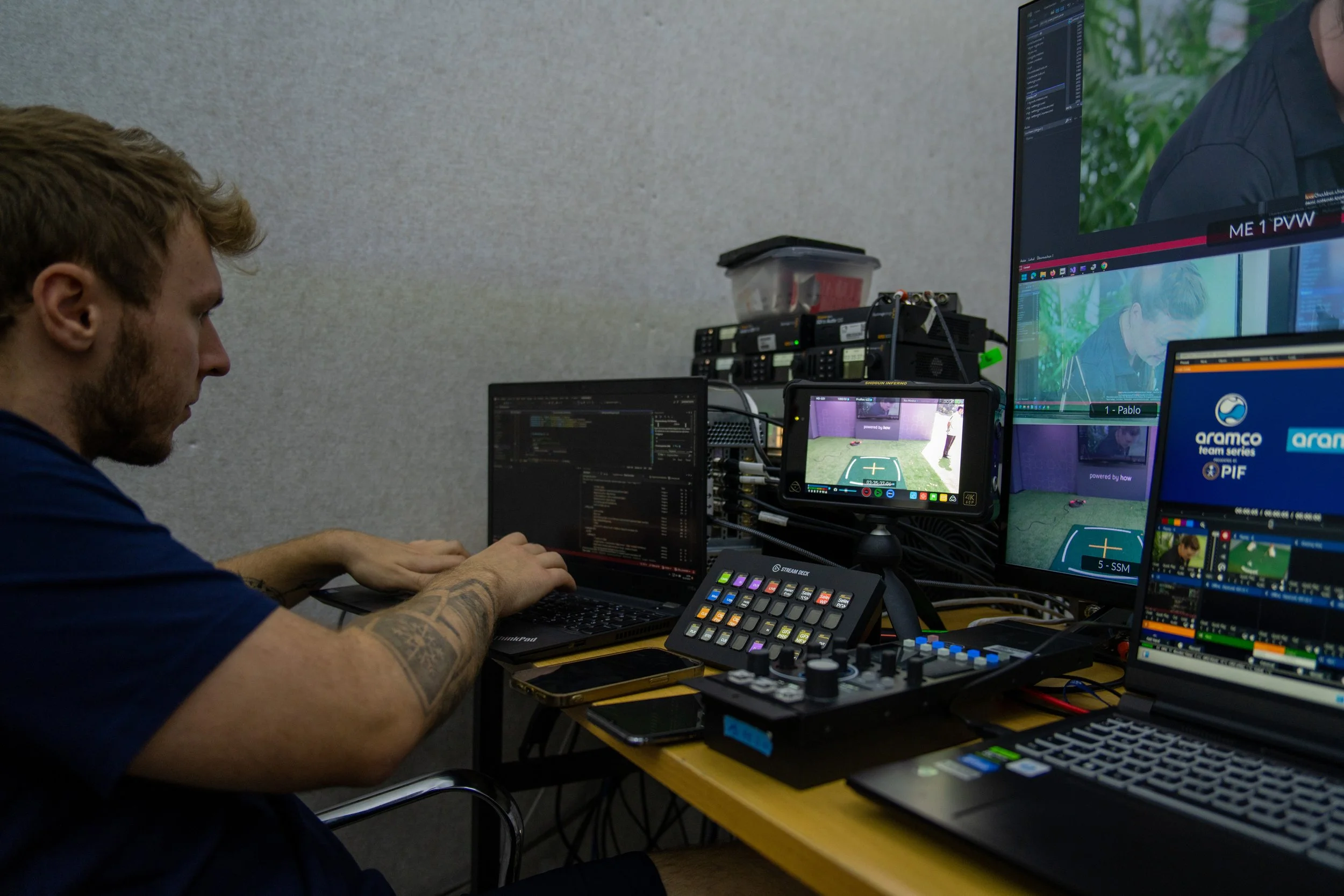 A person working on a computer with multiple screens and audio equipment, surrounded by video editing and streaming software.