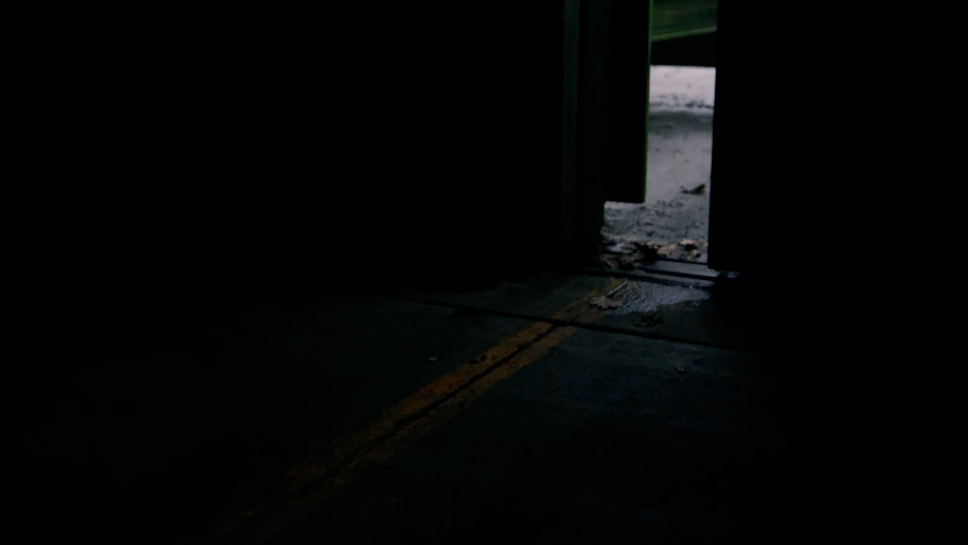 Dark indoor space with an open door showing an outdoor area with dirt and small rocks.