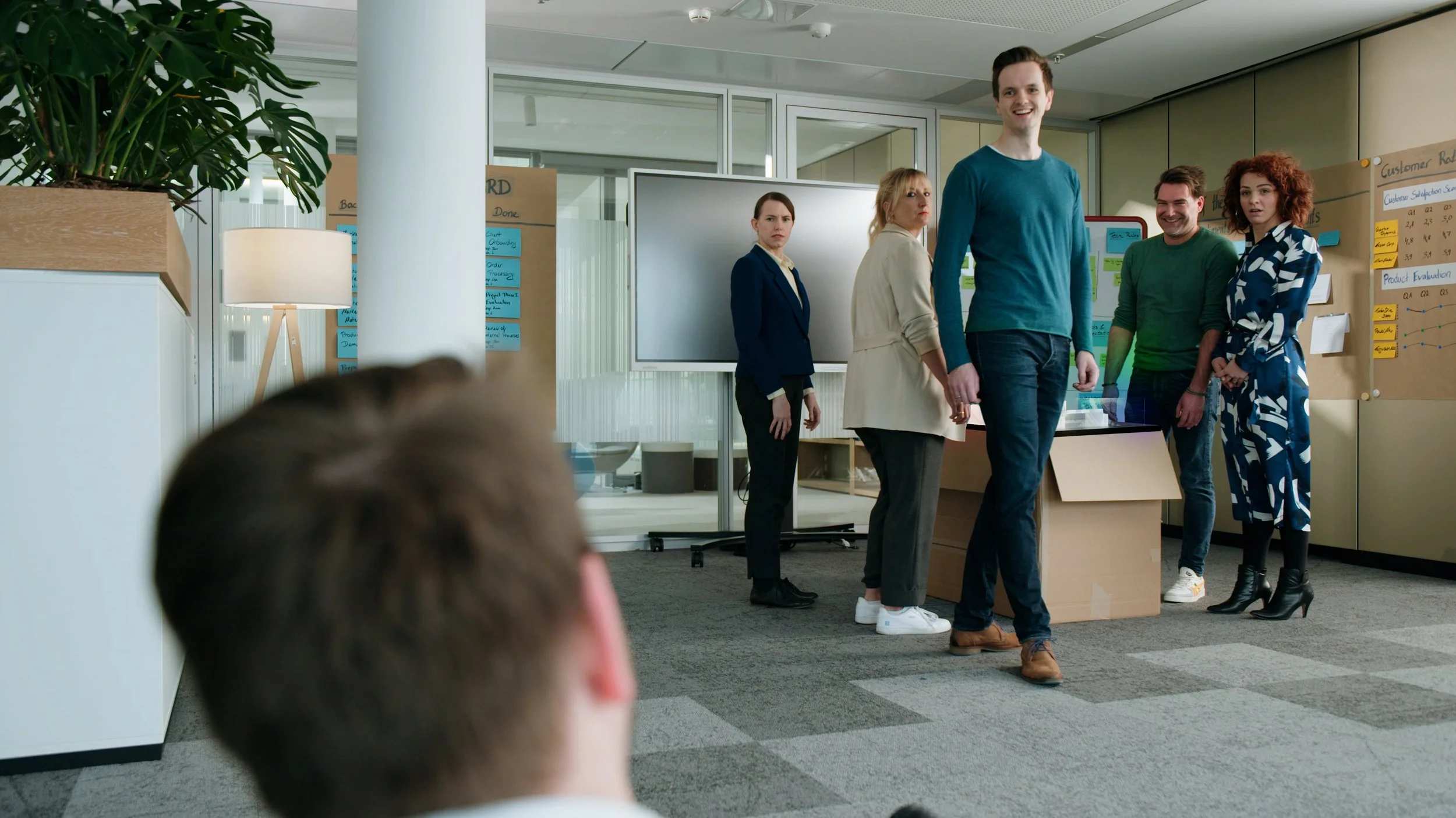 Young woman with blazer standing in front of a whiteboard in an office with four other people, who are listening to her presentation.