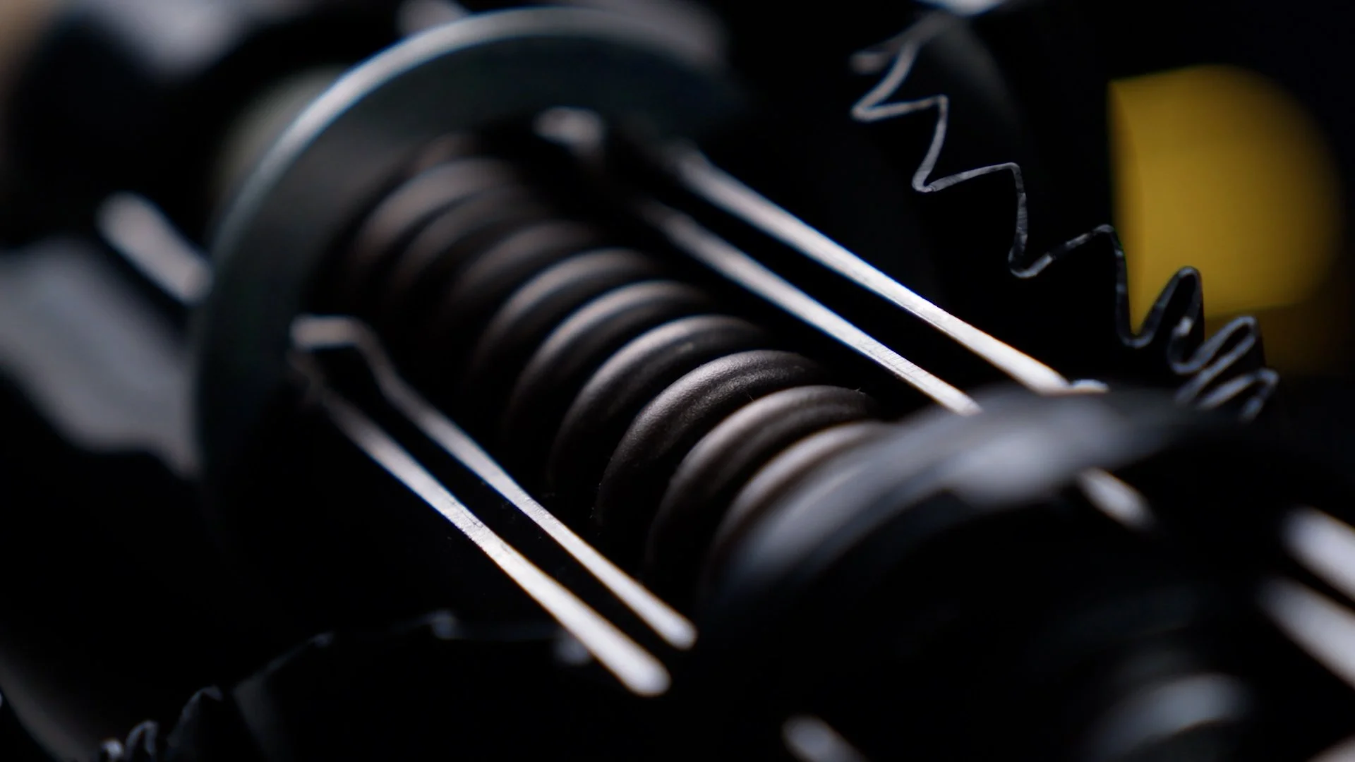 Close-up of metallic mechanical parts, including a coil and gears, with a yellow component in the background.