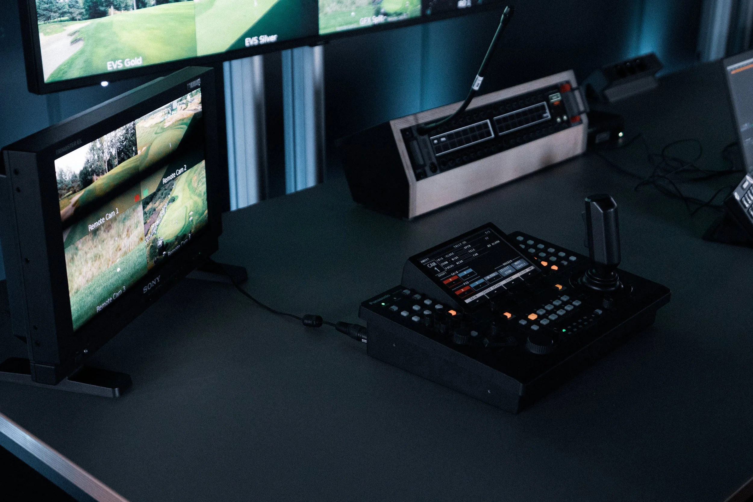 A golf course is displayed on multiple monitors in a control room, with a video editing or broadcast control console in the foreground.