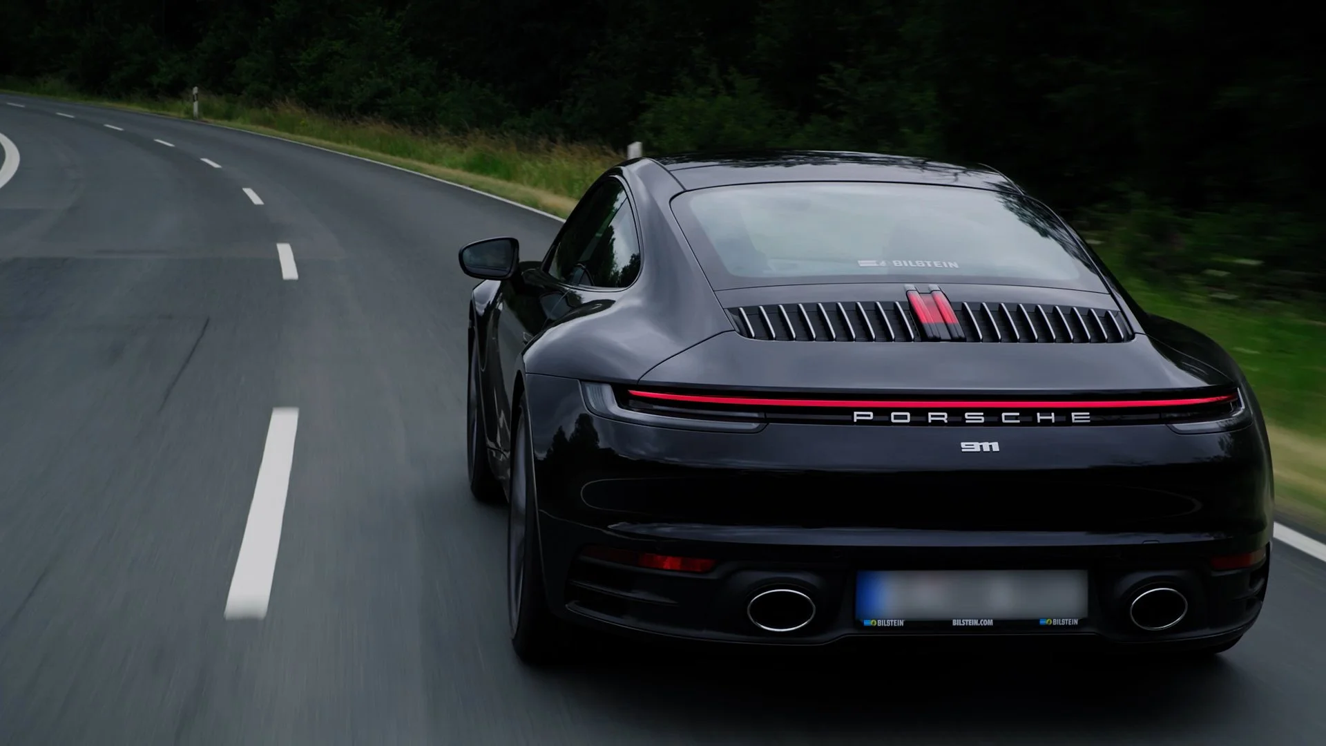 Black Porsche 911 driving on a winding road with trees on the side.