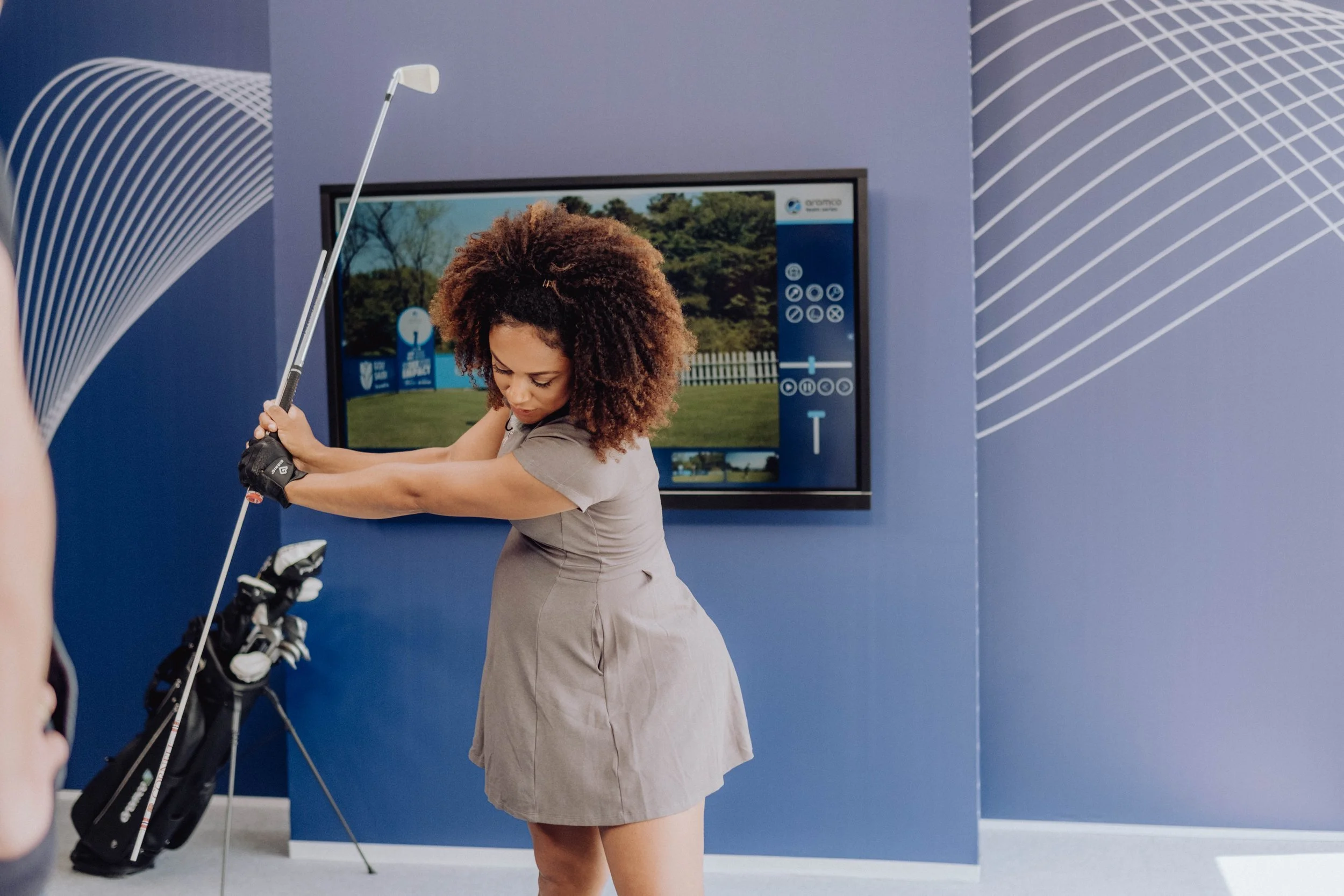 Woman practicing golf swing indoors with a golf simulator, displayed on a screen in the background.
