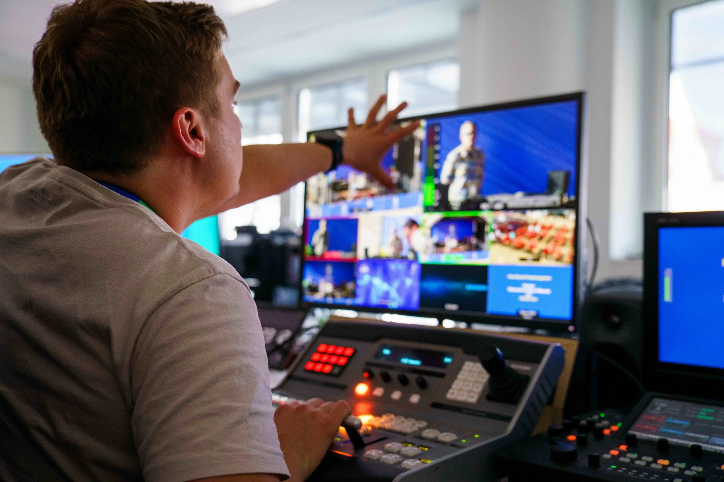 A person operating video production equipment with multiple monitors displaying a live feed of a person speaking.