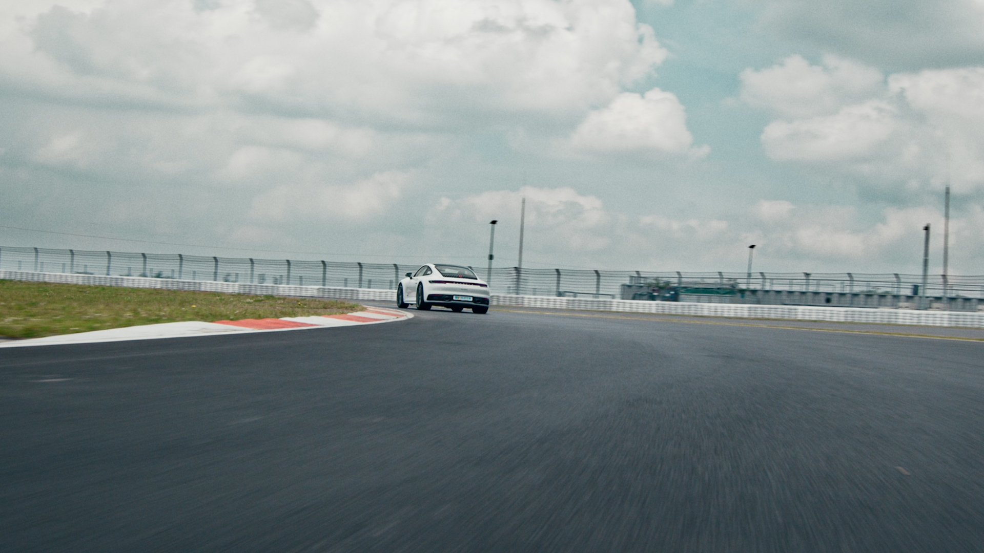 A white sports car driving on a racetrack curve with barriers and sky in the background.