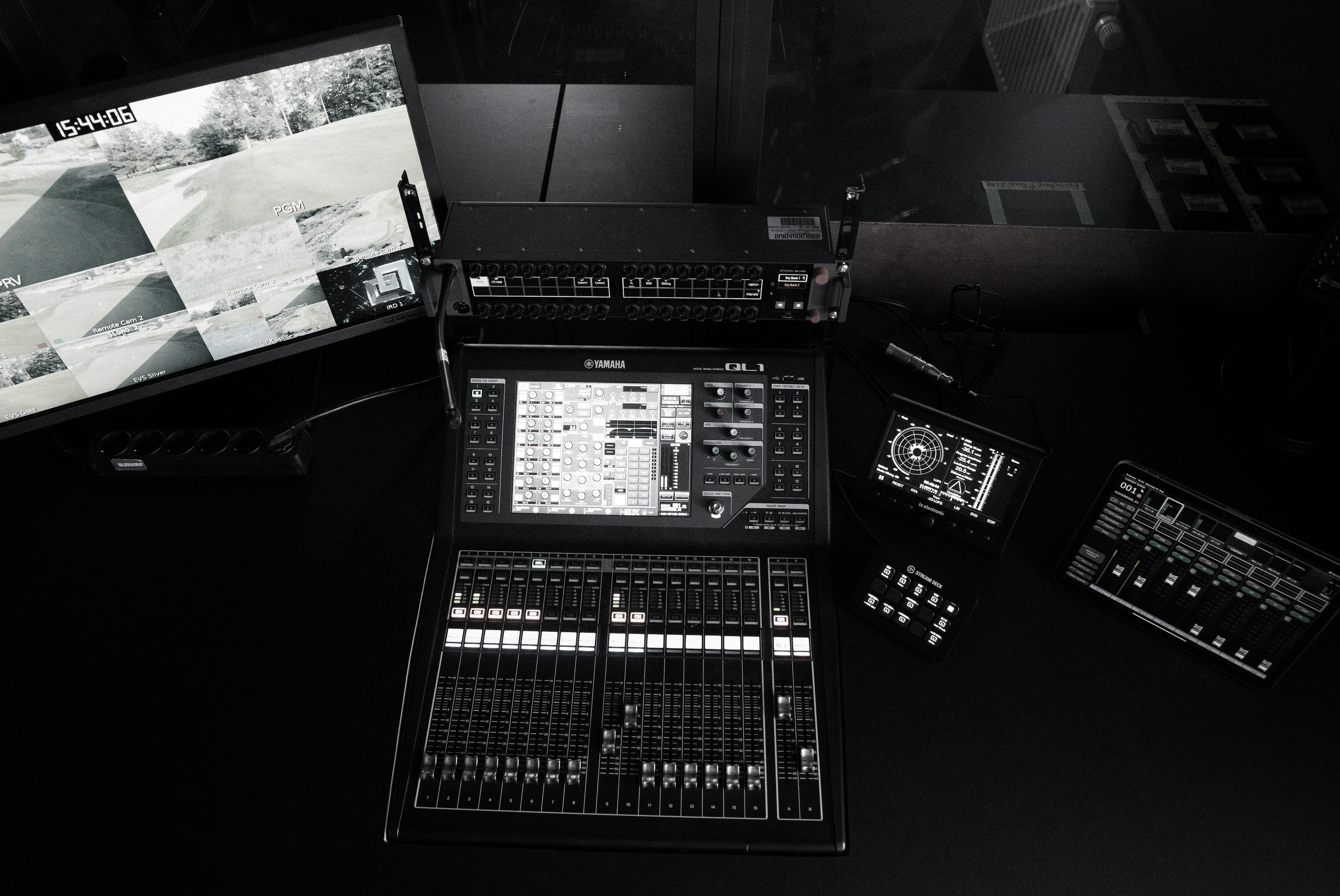 A professional audio mixing console with multiple sliders, knobs, and buttons, set in a dark studio environment with screens displaying visual interfaces.