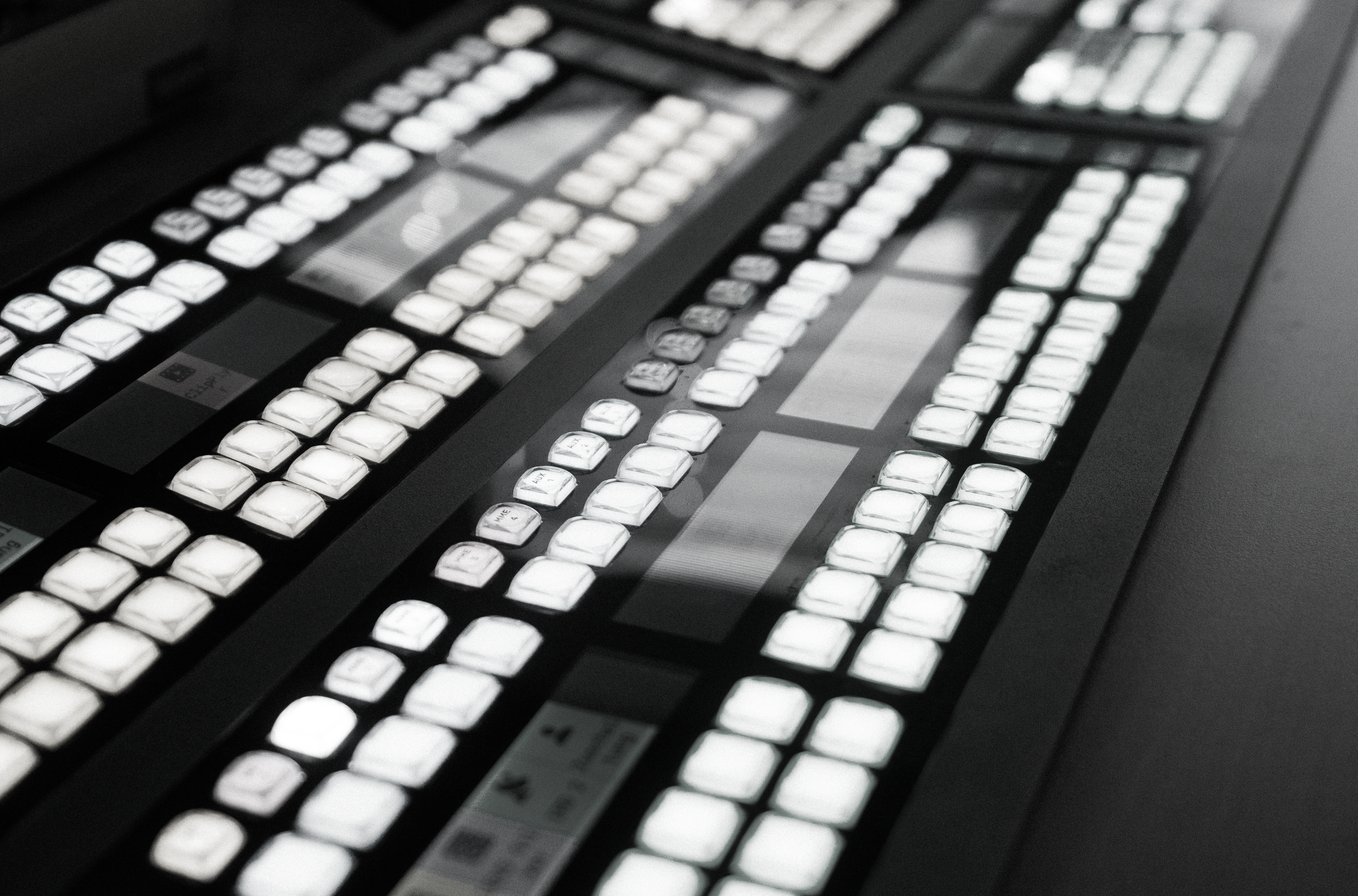 A professional video production switcher with multiple illuminated buttons and controls, used for live broadcasting or video editing.