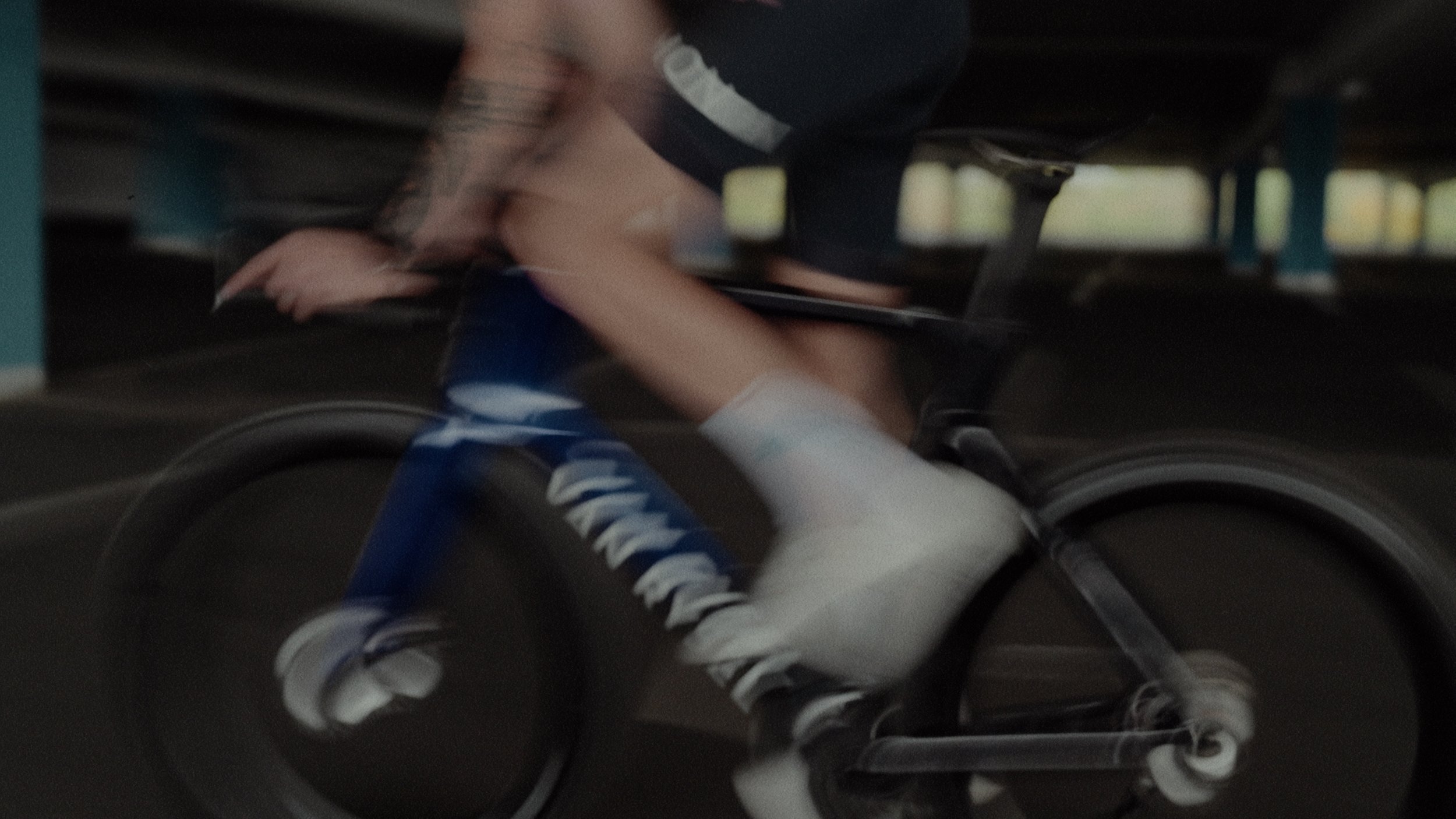 A person riding a bike inside a building, wearing blue sneakers, gray shorts, and a black shirt.