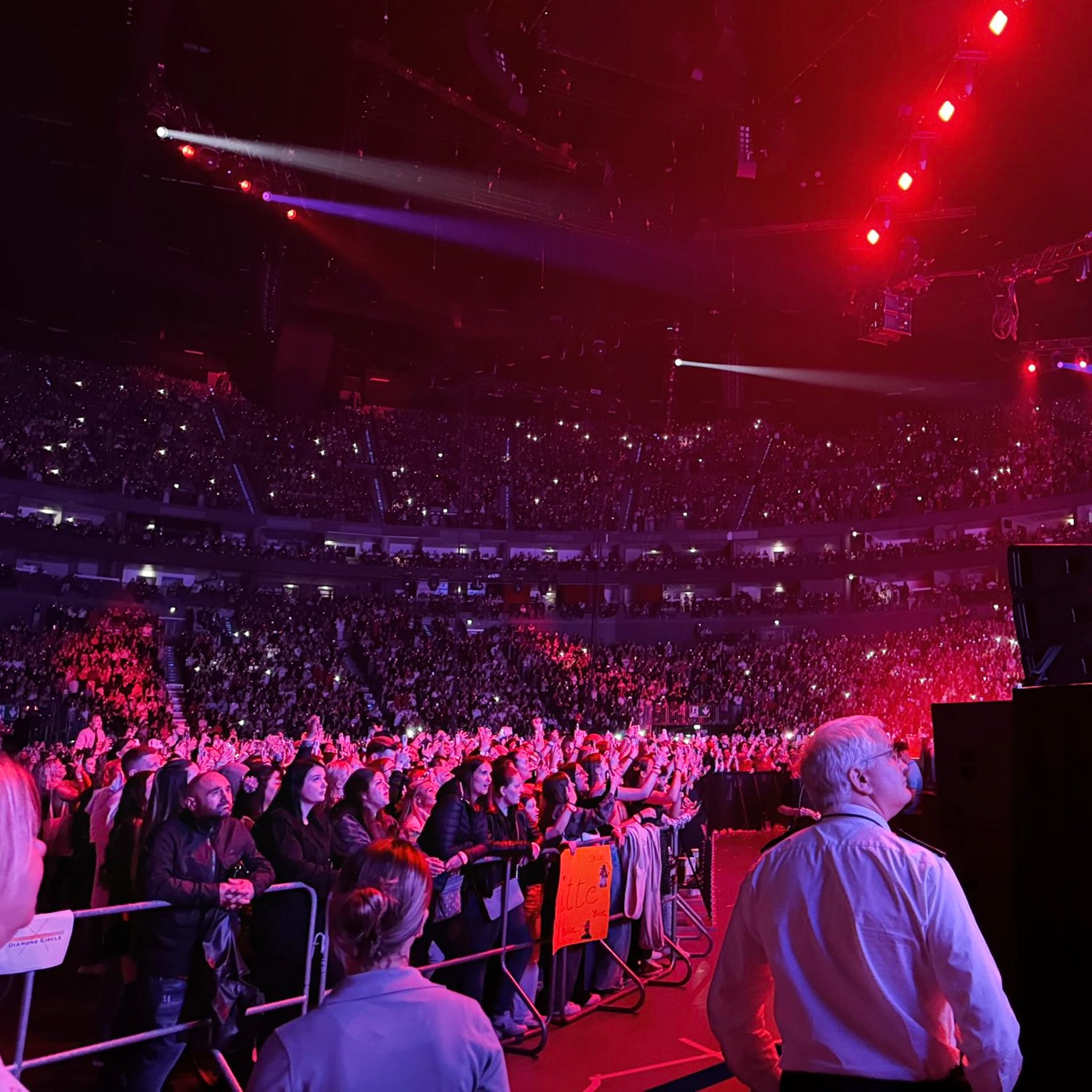 View of a large indoor concert with the audience and stage lighting.
