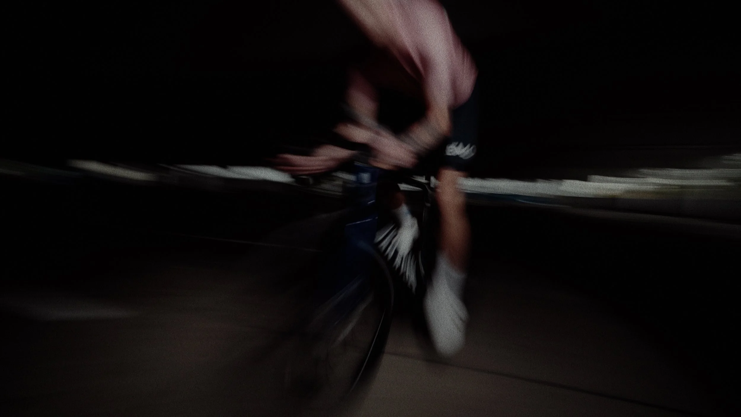 A person riding a bicycle at night, wearing a black shirt with white writing, illuminated by a light source.