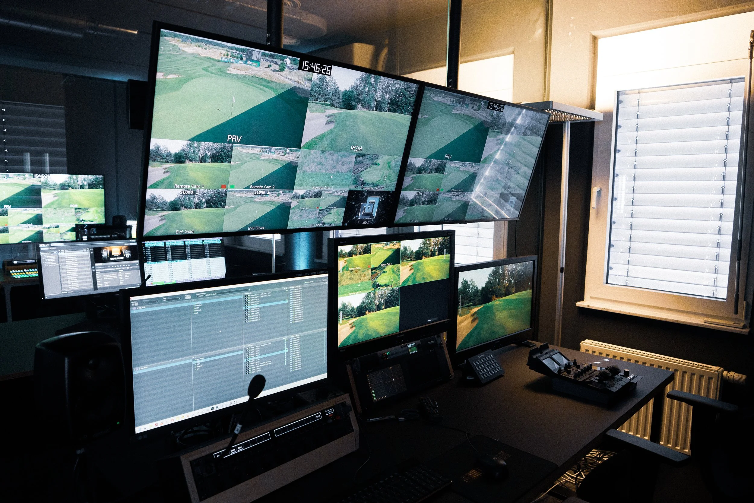 Golf course monitoring room with multiple screens displaying live golf course footage and control panels.