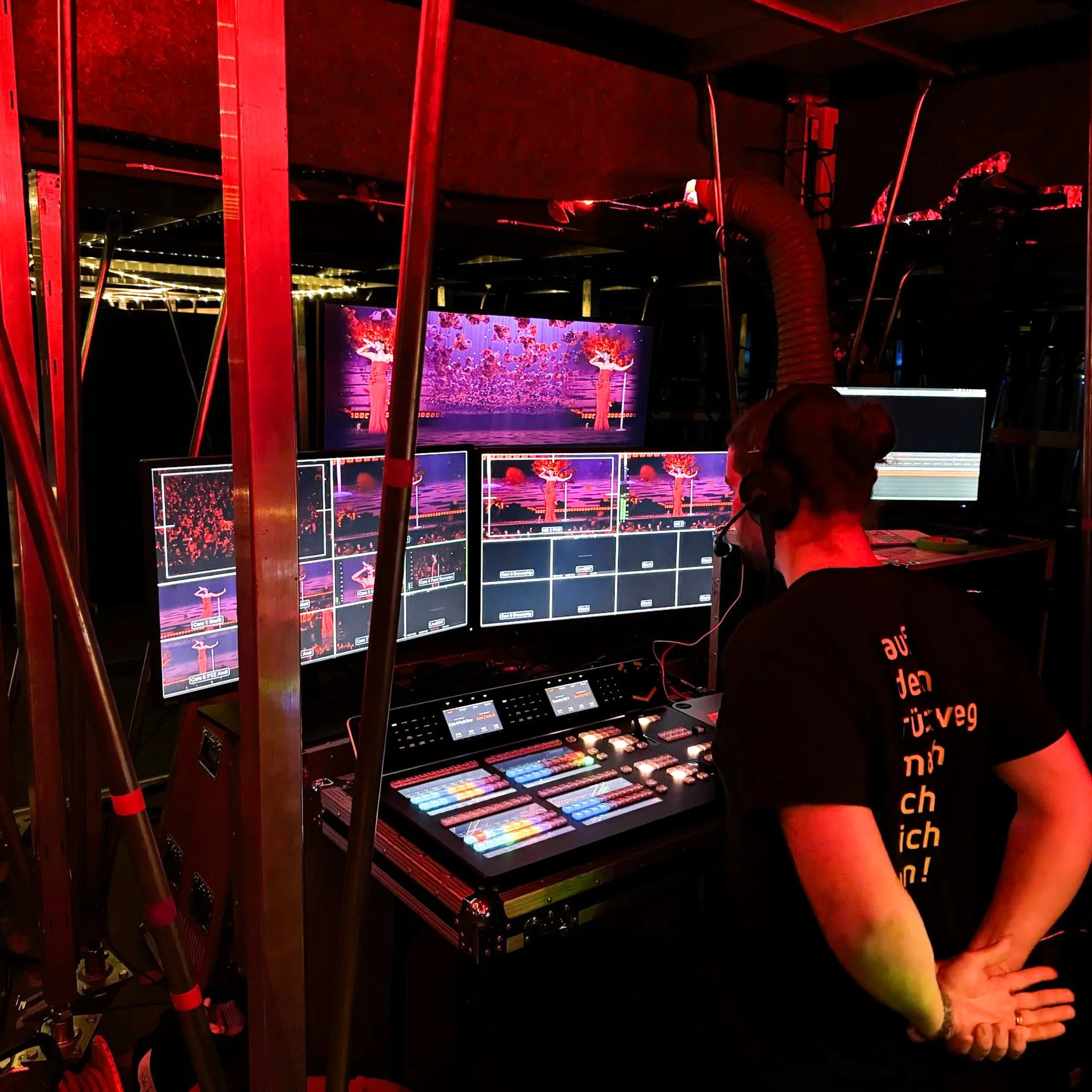A person operating a video switcher and monitor setup at a live event, displaying a colorful image of trees with red and pink blossoms.