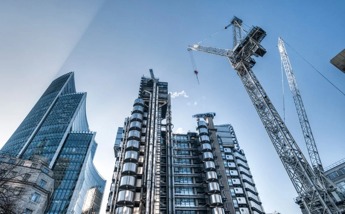 Construction cranes and tall skyscraper under construction with a clear blue sky in the background.