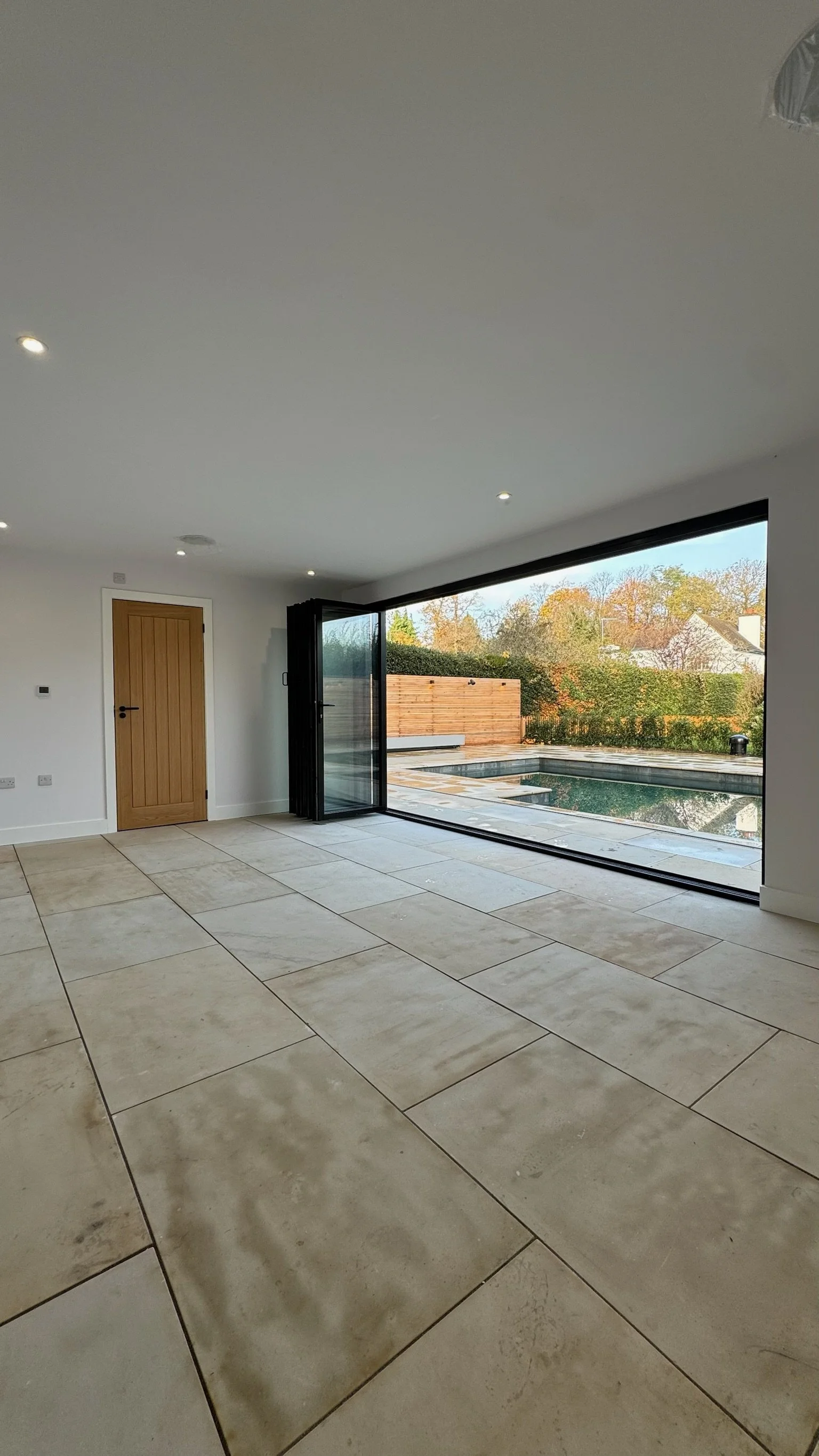 Empty room with large sliding glass doors opening to a backyard with a pool and trees