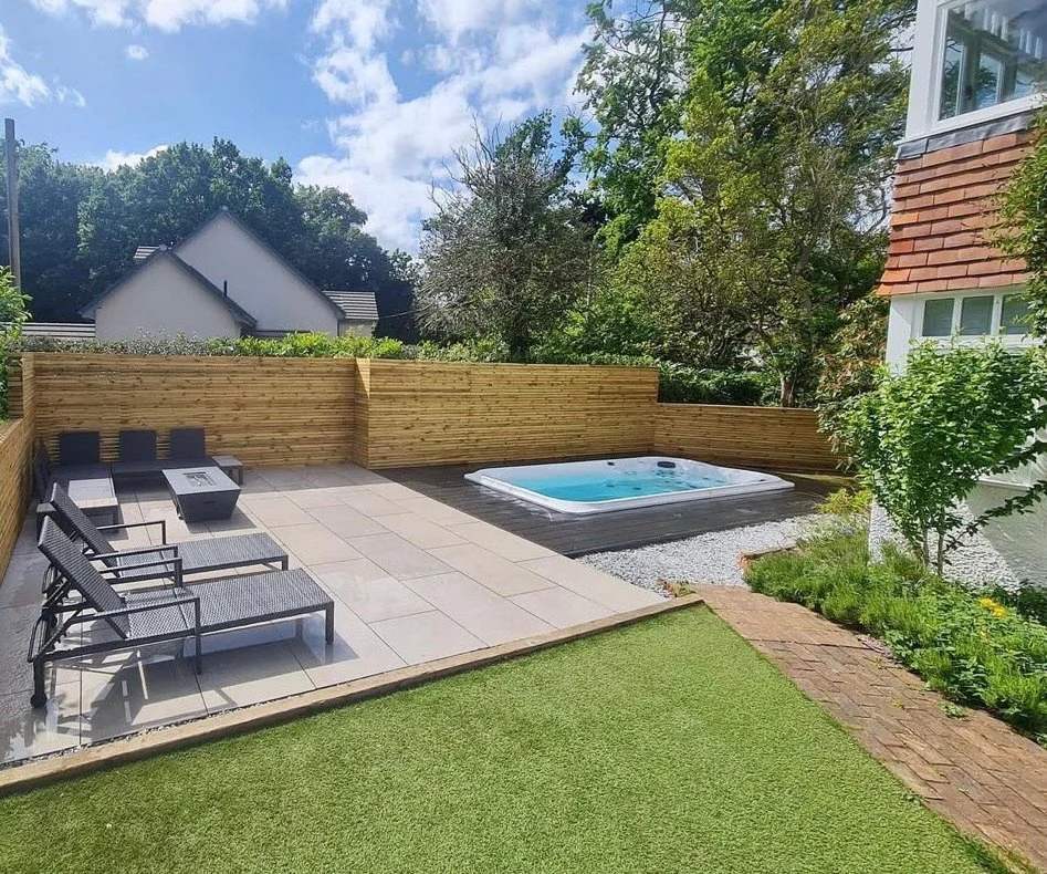 Backyard with a hot tub, outdoor seating, and a wooden privacy fence, surrounded by trees and a house with a partial porch.